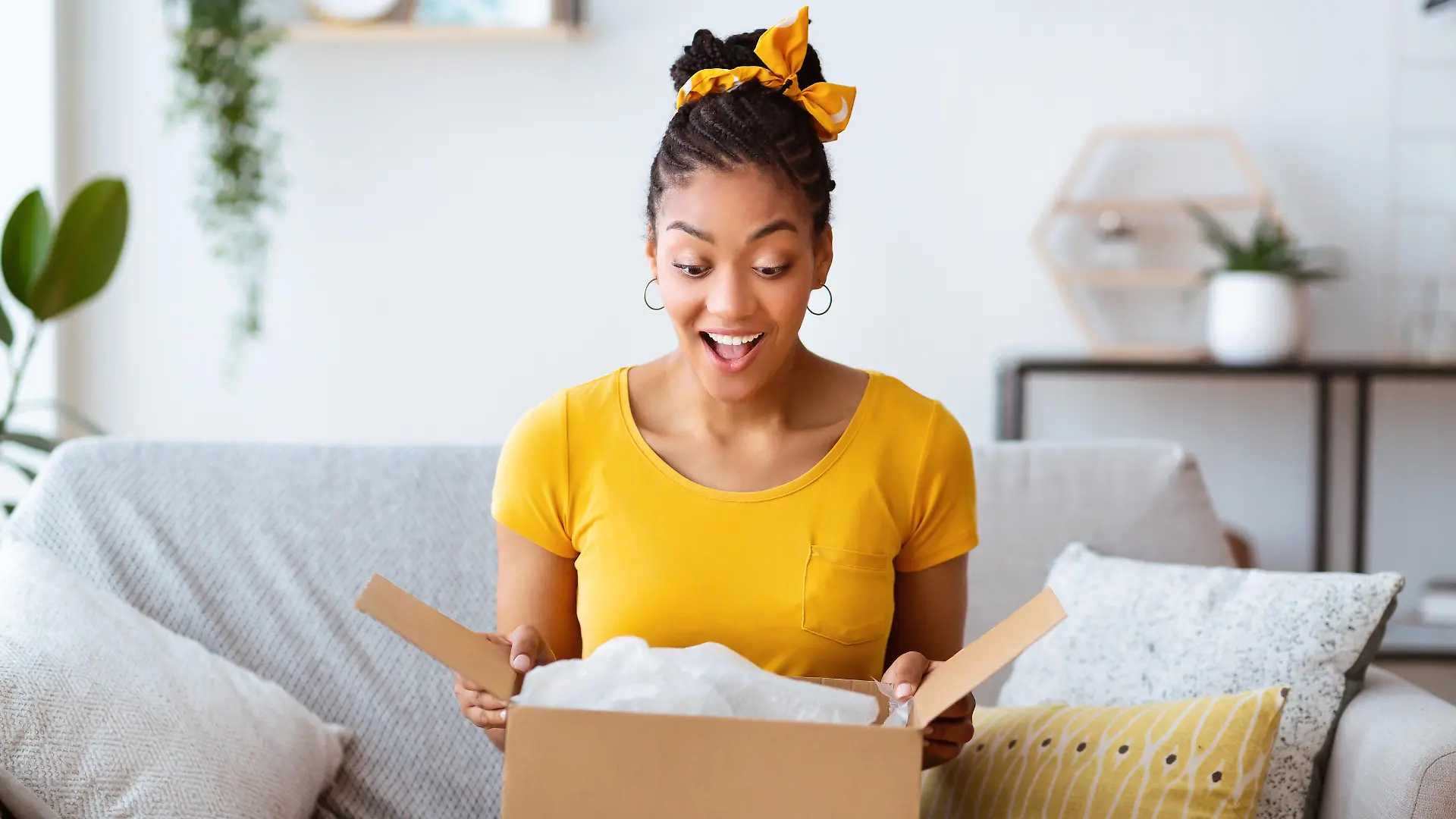 Buying Via Internet. Excited afro girl sitting on sofa unboxing cardboard delivery package, copy space