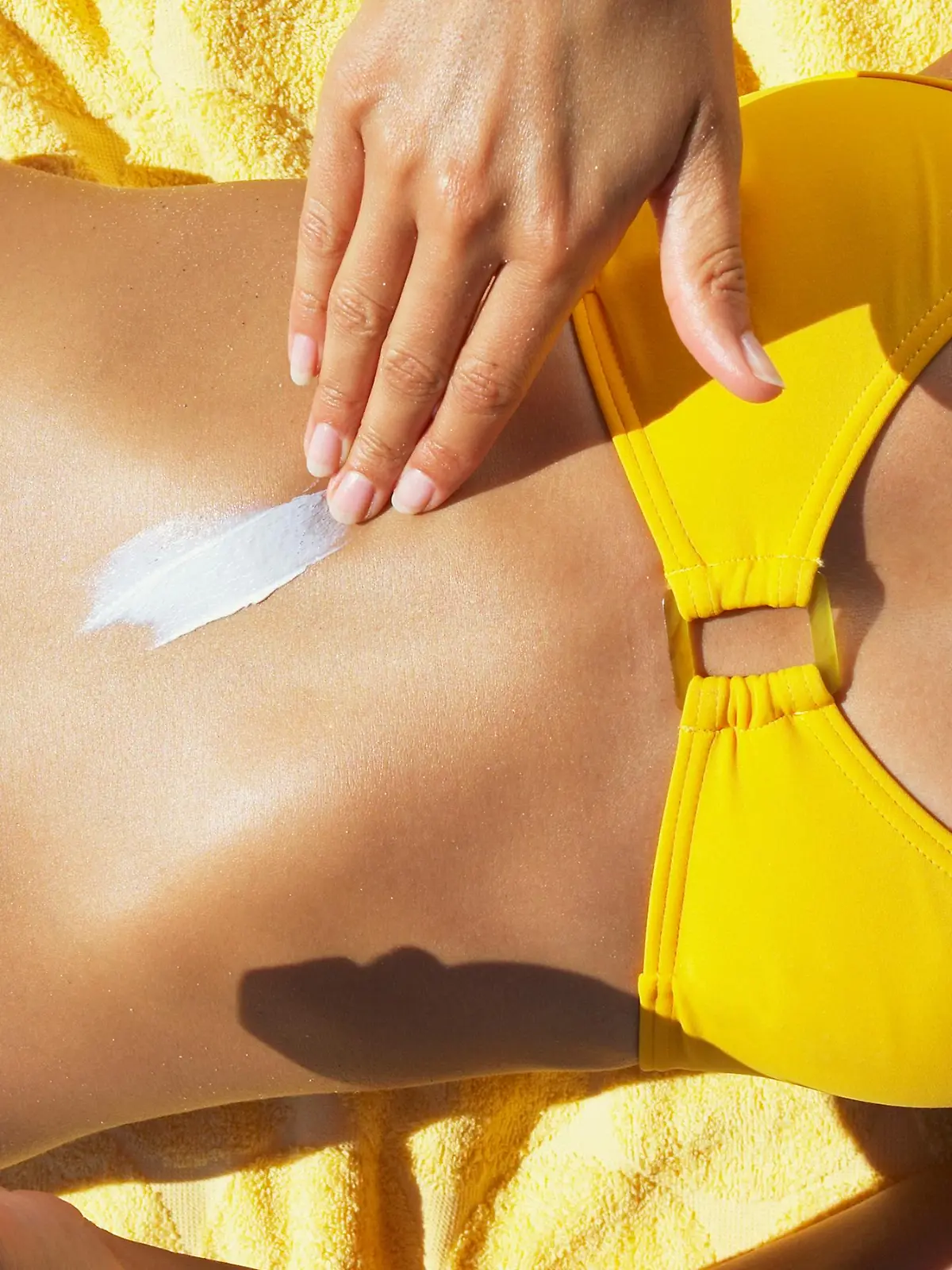 Frau im Bikini cremt sich den Bauch mit Sonnencreme ein