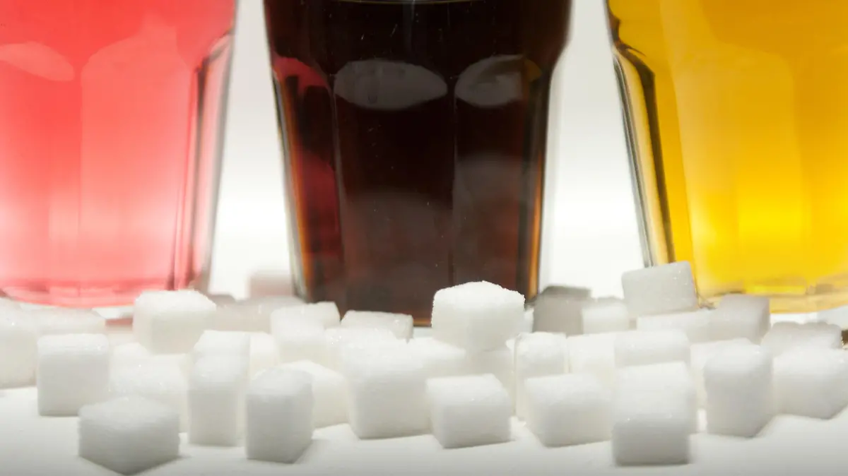 ARCHIV - ILLUSTRATION - Drei Gläser gefüllt mit roter Limonade, Cola und Energy-Drink stehen am 23.08.2016 in Berlin neben Zuckerwürfeln auf einem Tisch. Zucker hat viele Namen: Glukosesirup, Fruktose, Maltose oder Saccharose zum Beispiel. Klingt ungesund - aber ist es das auch? Ein Ernährungstrend dreht sich um die Abstinenz von dem «süßen Gift». (zu dpa "Vegan war gestern: Was steckt hinter dem Ernährungstrend Zuckerfrei?" vom 15.05.2017) Foto: Monika Skolimowska/dpa +++(c) dpa - Bildfunk+++