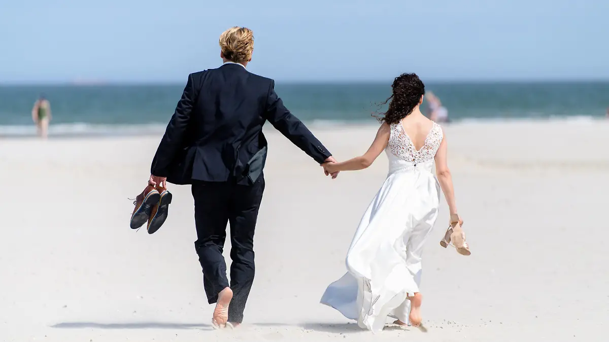 ARCHIV - 26.07.2019, Niedersachsen, Juist: Ein Brautpaar geht nach ihrer Trauung am Strand entlang. In Niedersachsen wird immer häufiger geheiratet. Foto: Matthias Balk/dpa +++ dpa-Bildfunk +++