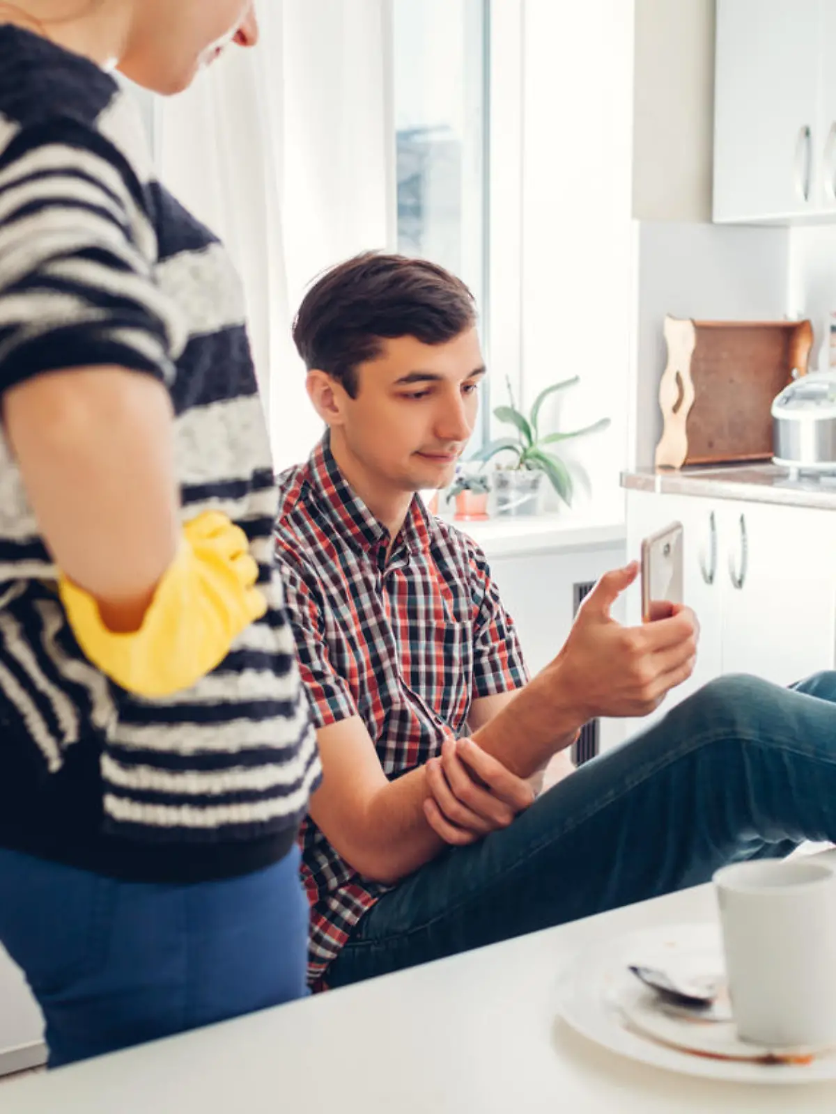 Lazy boyfriend hanging in phone while his girlfriend cleaning his dishes after dinner in kitchen. Inequality of men's and women's rights. Family conflict