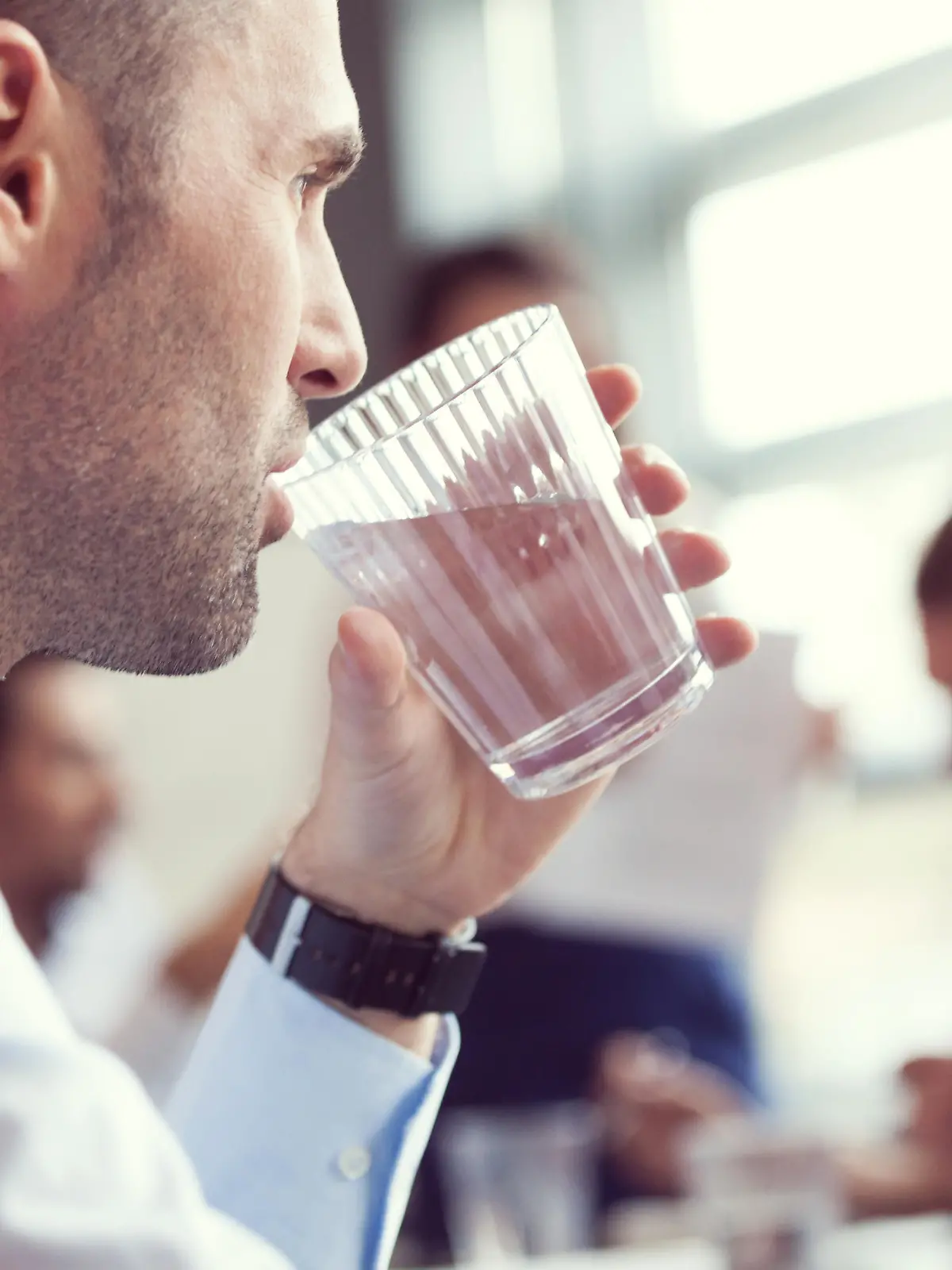 Close up of businessman drinking water at the meeting.  In the background blured business team discussing in a board room in an office.