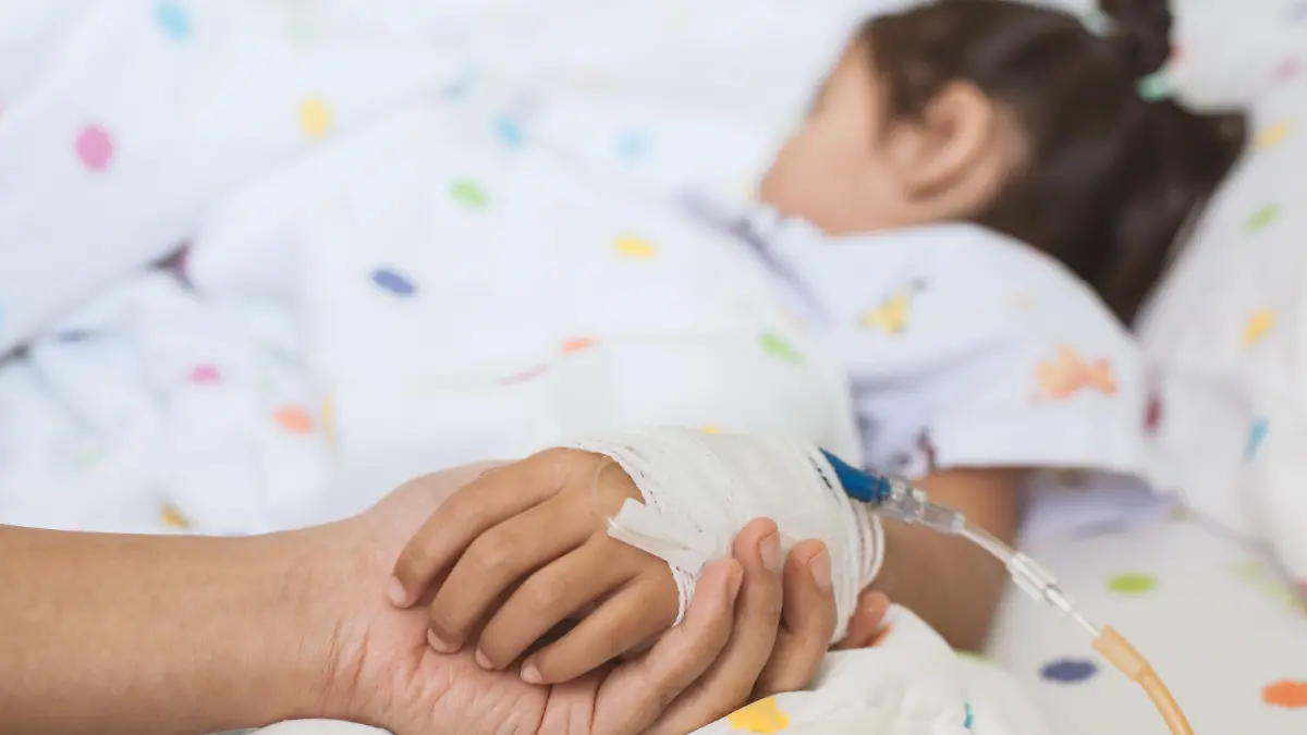 Mother hand holding sick daughter hand who have IV solution bandaged with love and care while she is sleeping on bed in the hospital