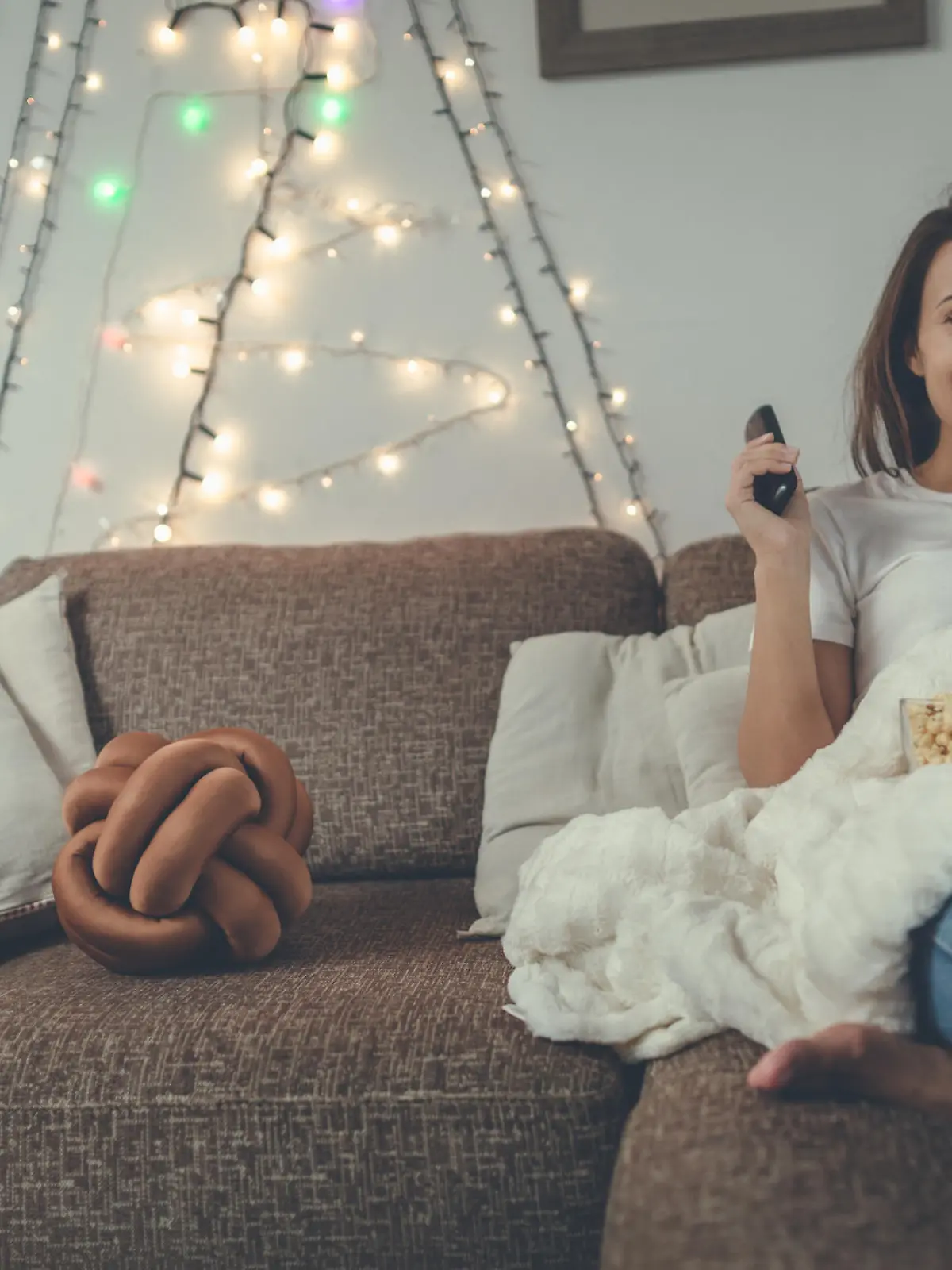 Good-looking girl is wearing blue jeans and white t-shirt. She feels relaxed. While she is watching TV shows she is eating popcorn.