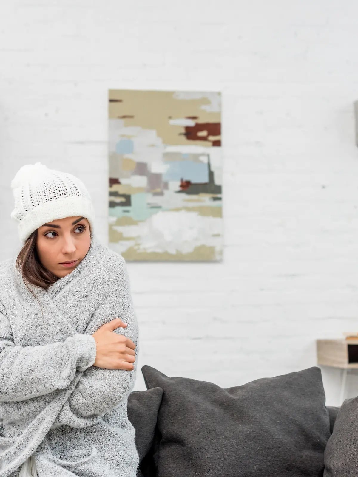 freezed young woman in warm clothes sitting on couch at home with air condition hanging on background