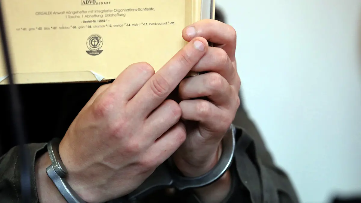 dpatopbilder - 24.09.2019, Mecklenburg-Vorpommern, Neubrandenburg: Vor Beginn des Prozesses wegen Mordes durch Unterlassen und Misshandlung von Schutzbefohlenen in sieben Fällen hält sich der angeklagte Stiefvater einen Aktendeckel vor das Gesicht und zeigt in Richtung Anklage einen "Stinkefinger", der offensichtlich dem Vater der getöten Leonie gilt, der ihn laut beschimpft. Der Beschuldigte soll Leonie schwer misshandelt und keine medizinische Hilfe geholt haben, um nicht aufzufliegen. Das Kind starb unter anderem an schweren Kopfverletzungen und war am 12. Januar tot in der Wohnung der Familie gefunden worden. Foto: Bernd Wüstneck/dpa-Zentralbild/dpa +++ dpa-Bildfunk +++