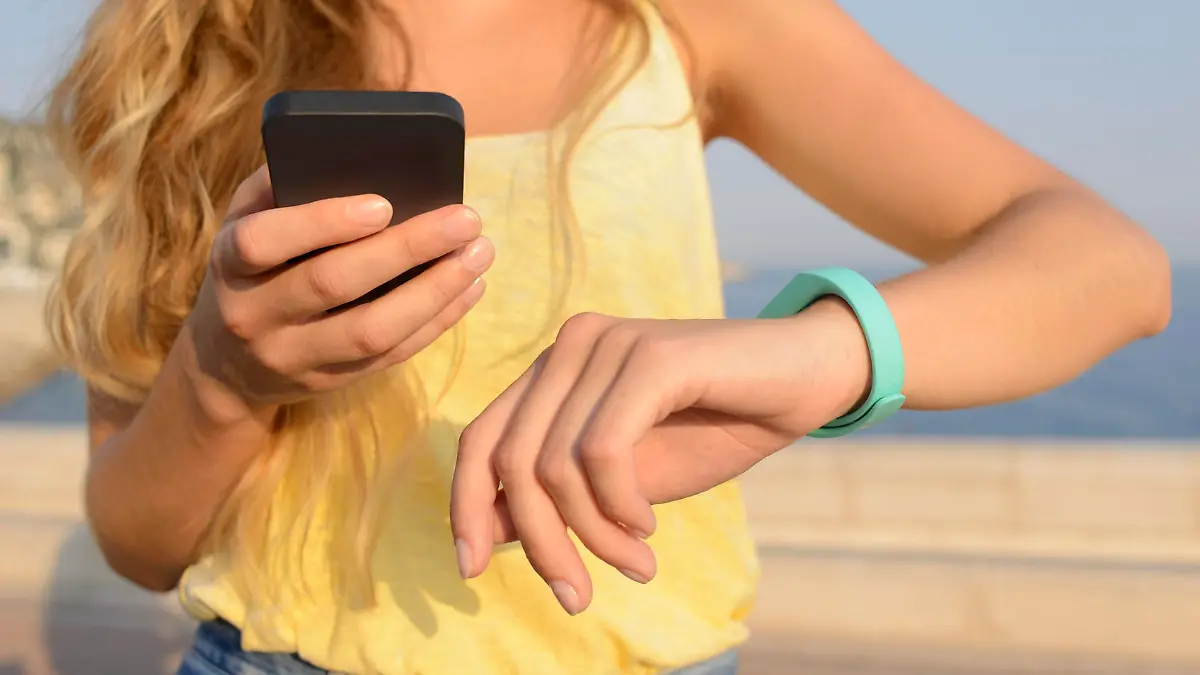 Slim young woman in summer attire using a fitness activity tracking device and smart phone while walking outdoors. Shot on a summer evening in Nice, France, with the Mediterranean Sea in the background.