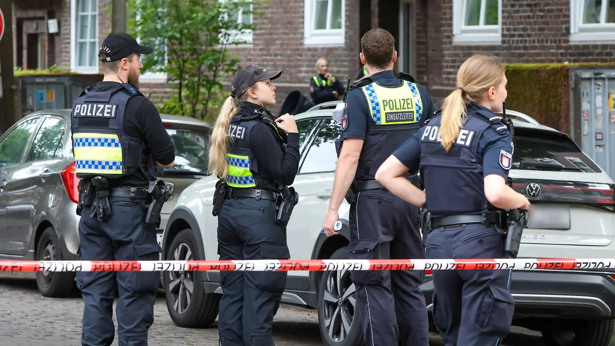 Einsatzkräfte der Polizei sichern eine Straße an einem Mehrfamilienhaus in Hamburg-Barmbek.