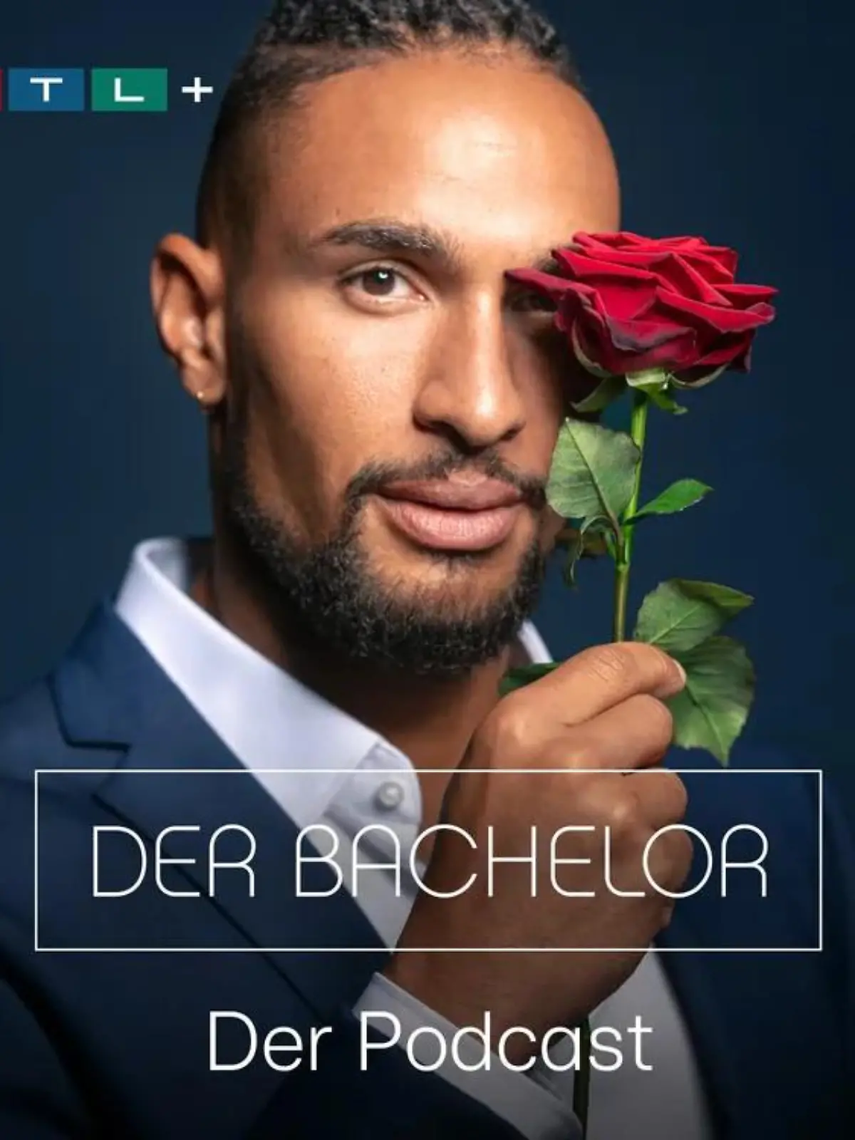 Auf dem Bild ist der aktuelle Bachelor mit einer Rose in der Hand zu sehen. Er trägt einen blauen Anzug