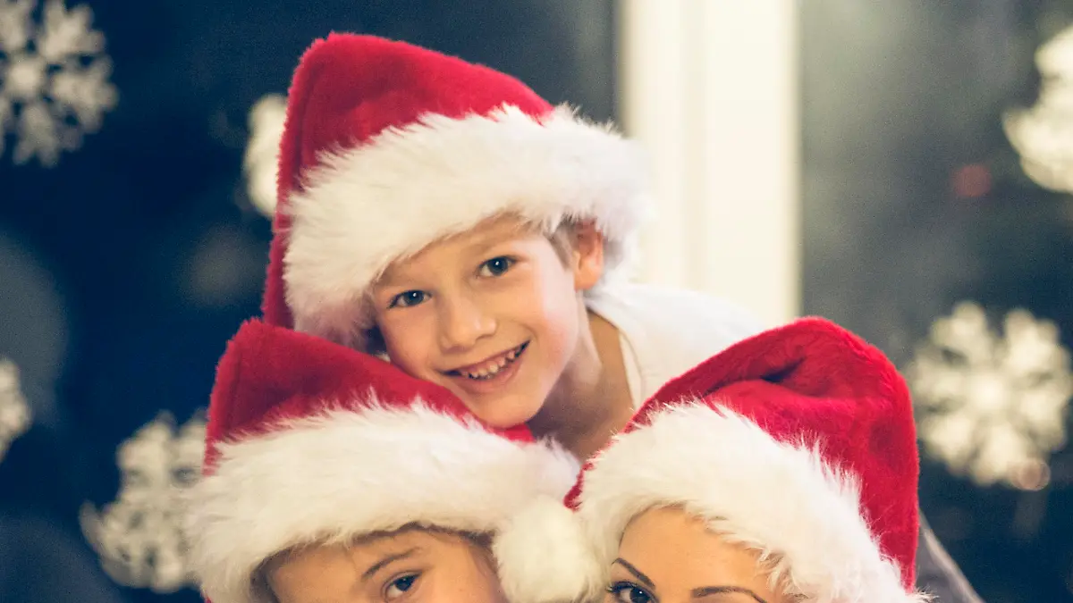 Happy family with two children with Santa hats lying down on the floor, looking at camera.