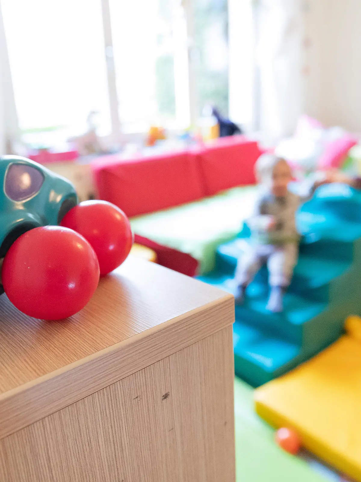 ARCHIV - 03.03.2020, Nordrhein-Westfalen, Bielefeld: ILLUSTRATION - Ein Spielzeugauto ist in den Räumen einer Kindertagesstätte zu sehen. Im Hintergrund ein Kind zusammen mit einer Erzieherin. Kinder in Nordrhein-Westfalen und anderen Bundesländern werden in der Corona-Krise nicht zu einem bundeseinheitlichen Stichtag in die Kitas zurückkehren. Das stellte NRW-Familienminister Stamp (FDP) am Montag klar. Foto: Friso Gentsch/dpa +++ dpa-Bildfunk +++