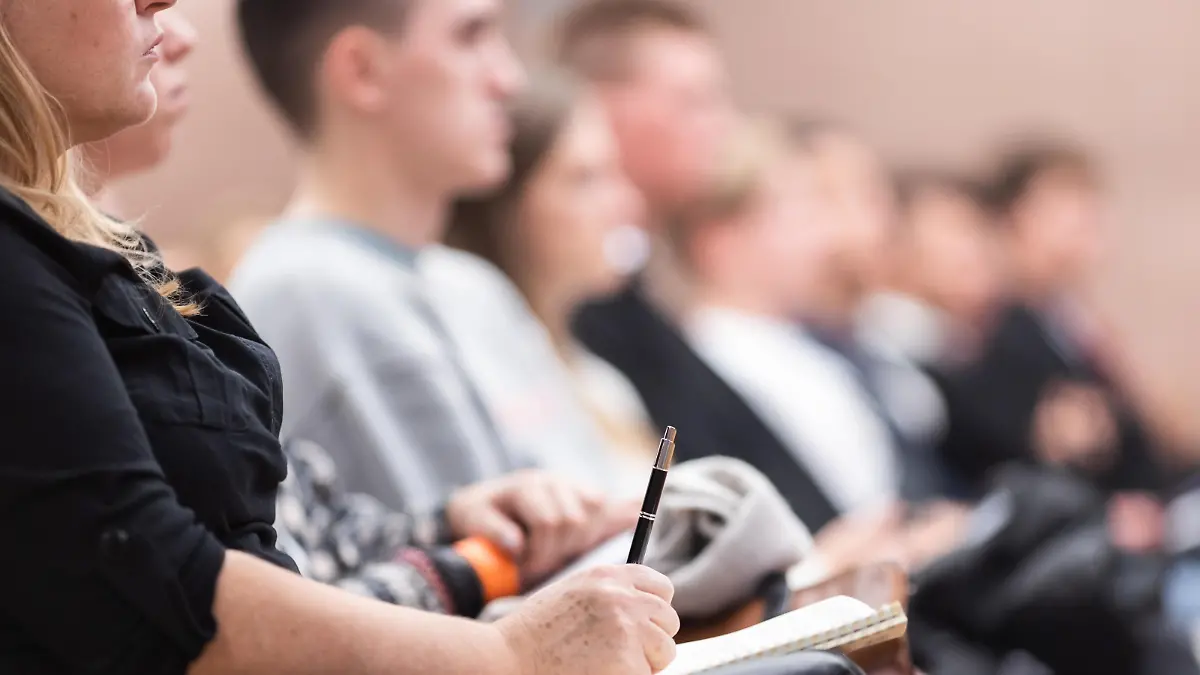 Female hands holding pen and notebook, making notes at conference lecture. Event participants in conference hall