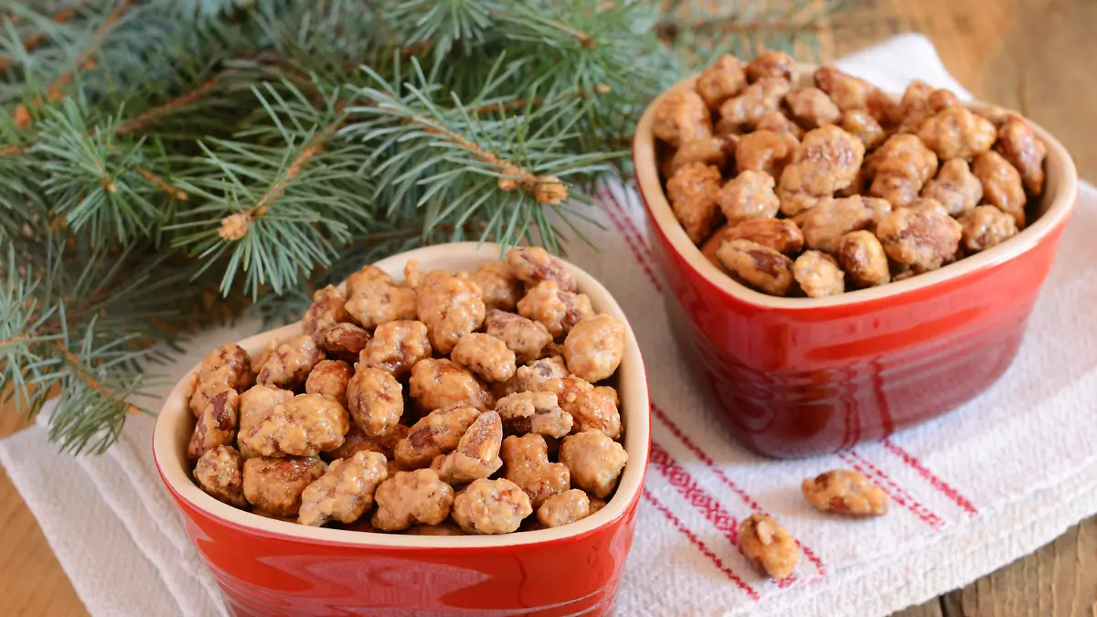 Christmas decoration with caramelized almond in red heart shaped bowls and fir tree branches on wooden background