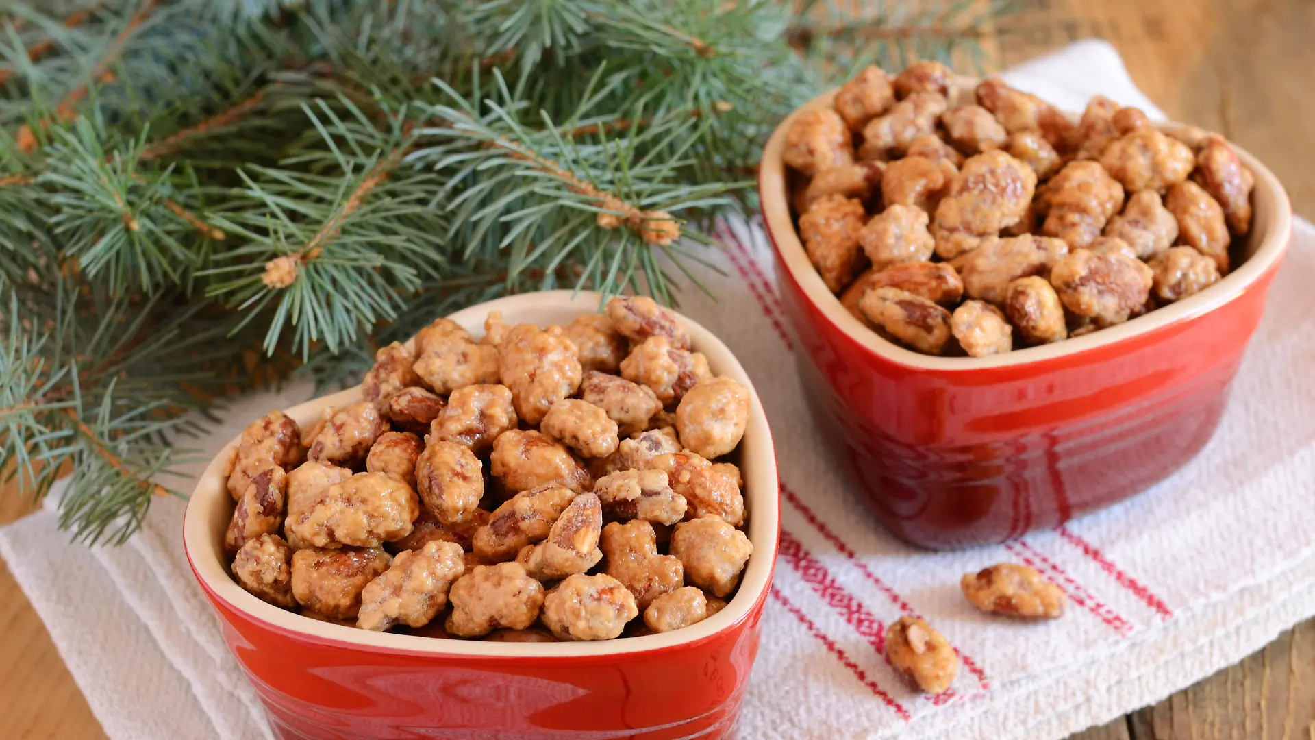 Christmas decoration with caramelized almond in red heart shaped bowls and fir tree branches on wooden background