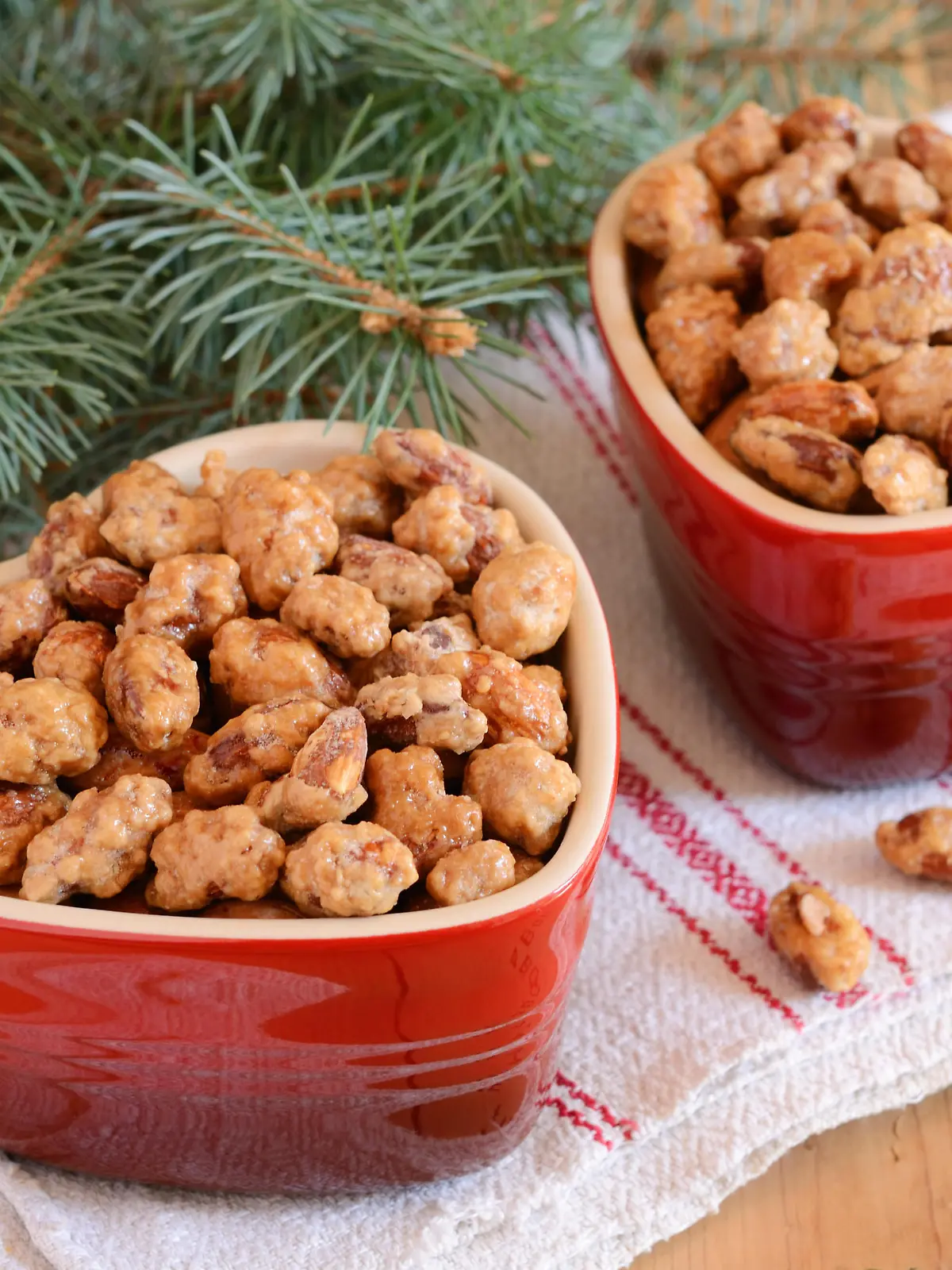 Christmas decoration with caramelized almond in red heart shaped bowls and fir tree branches on wooden background