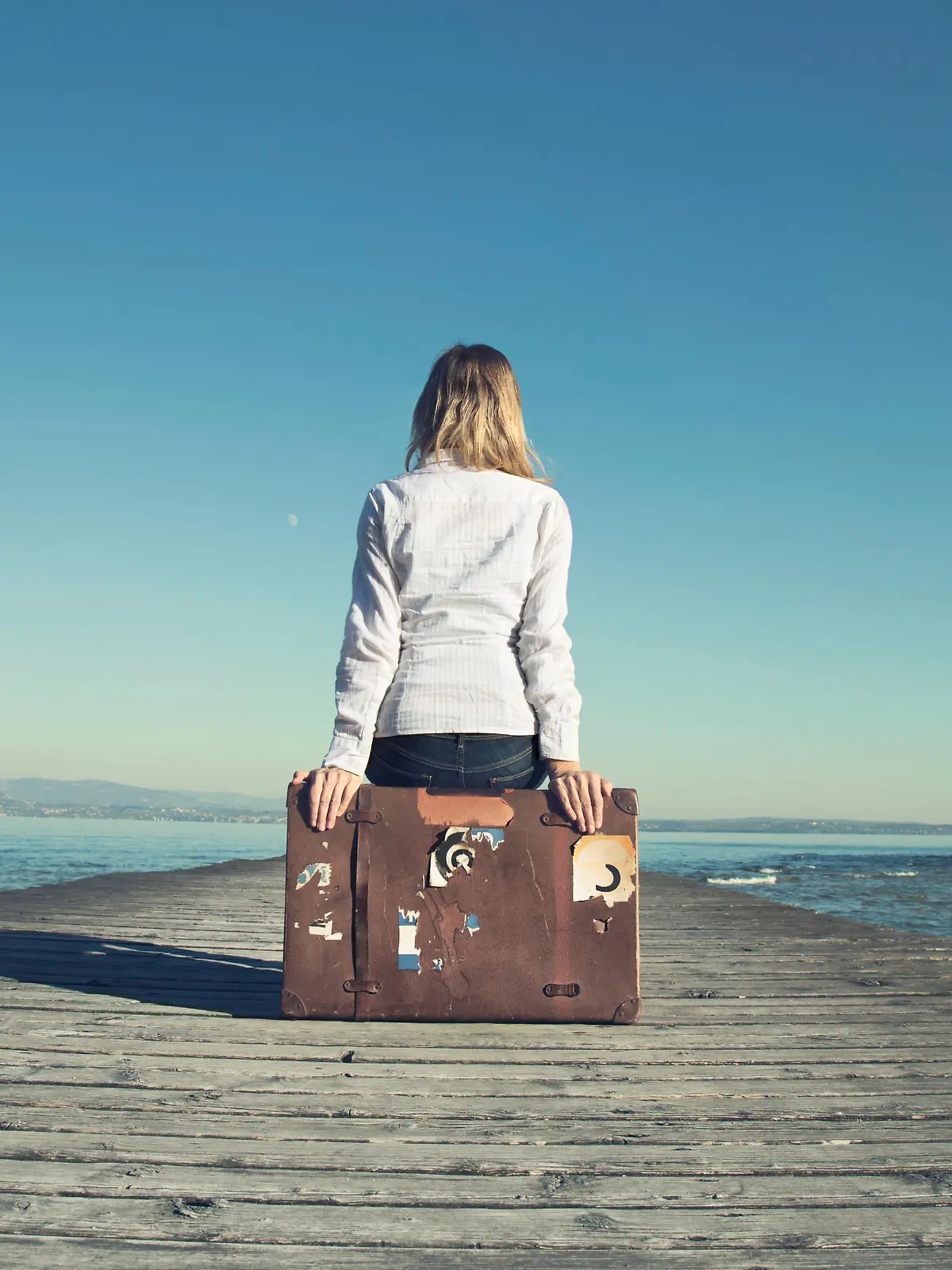 woman sitting on her suitcase waiting for the sunset in a spectacular view