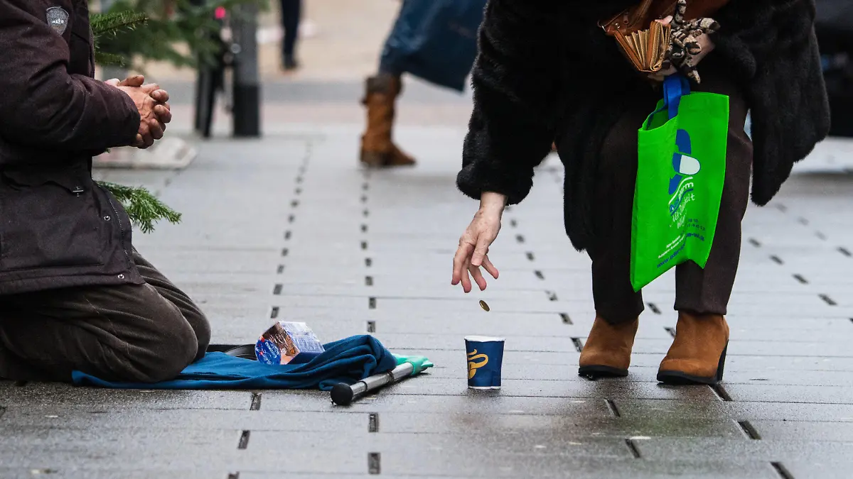 ARCHIV - 27.12.2017, Hessen, Wiesbaden: Eine Frau wirft einem Bettler ein Geldstück in einen Becher. Menschen ohne festen Wohnsitz sind nicht unbedingt die Wunschkunden vieler Banken. Mittlerweile haben sie aber das Recht auf ein Konto. (Zu dpa «Studie: Konten für Wohnungslose und Geflüchtete oft besonders teuer») Foto: Andreas Arnold/dpa +++ dpa-Bildfunk +++