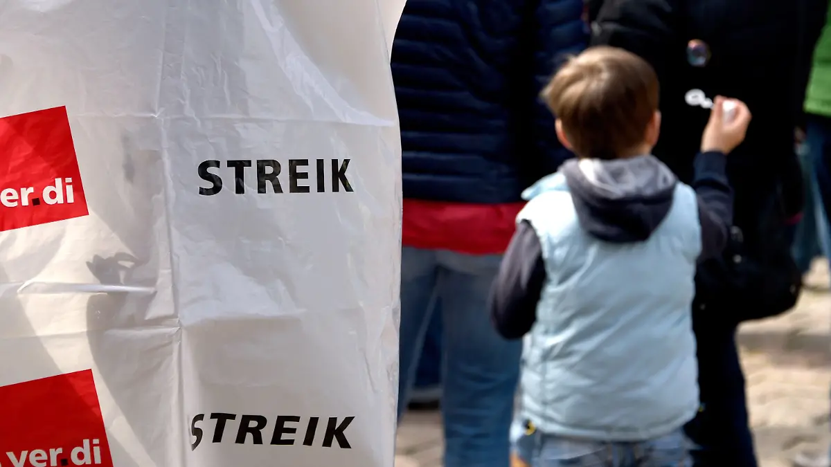Ein Junge steht am 08.05.2015 vor dem Rathaus in Kiel (Schleswig-Holstein) neben streikende Mitarbeitern von Kindertagesstätten. Viele Kitas in Schleswig-Holstein und Hamburg sind am Freitag geschlossen geblieben. Die Erzieherinnen beteiligten sich an unbefristeten Streiks. Foto: Carsten Rehder/dpa +++(c) dpa - Bildfunk+++