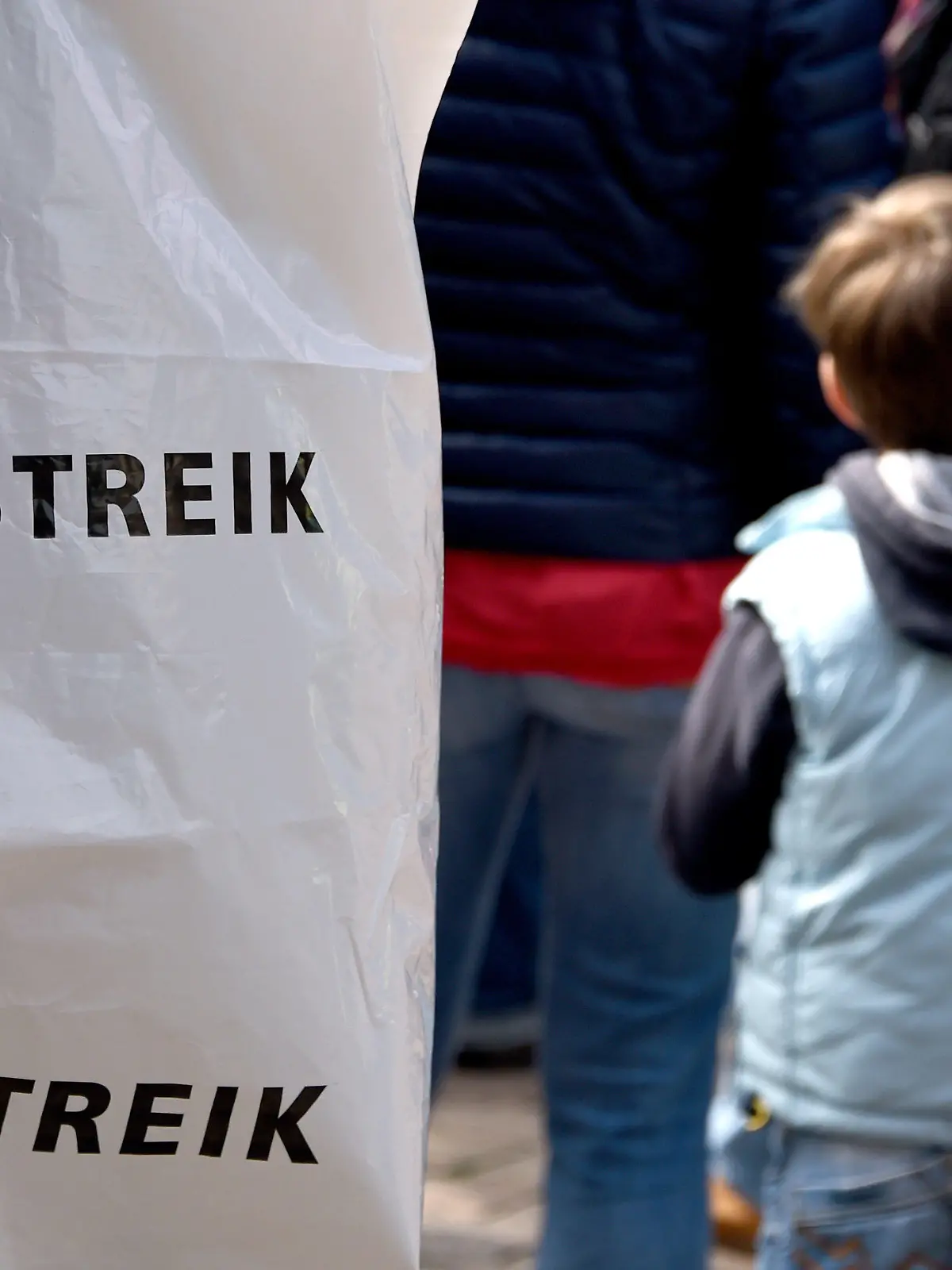 Ein Junge steht am 08.05.2015 vor dem Rathaus in Kiel (Schleswig-Holstein) neben streikende Mitarbeitern von Kindertagesstätten. Viele Kitas in Schleswig-Holstein und Hamburg sind am Freitag geschlossen geblieben. Die Erzieherinnen beteiligten sich an unbefristeten Streiks. Foto: Carsten Rehder/dpa +++(c) dpa - Bildfunk+++
