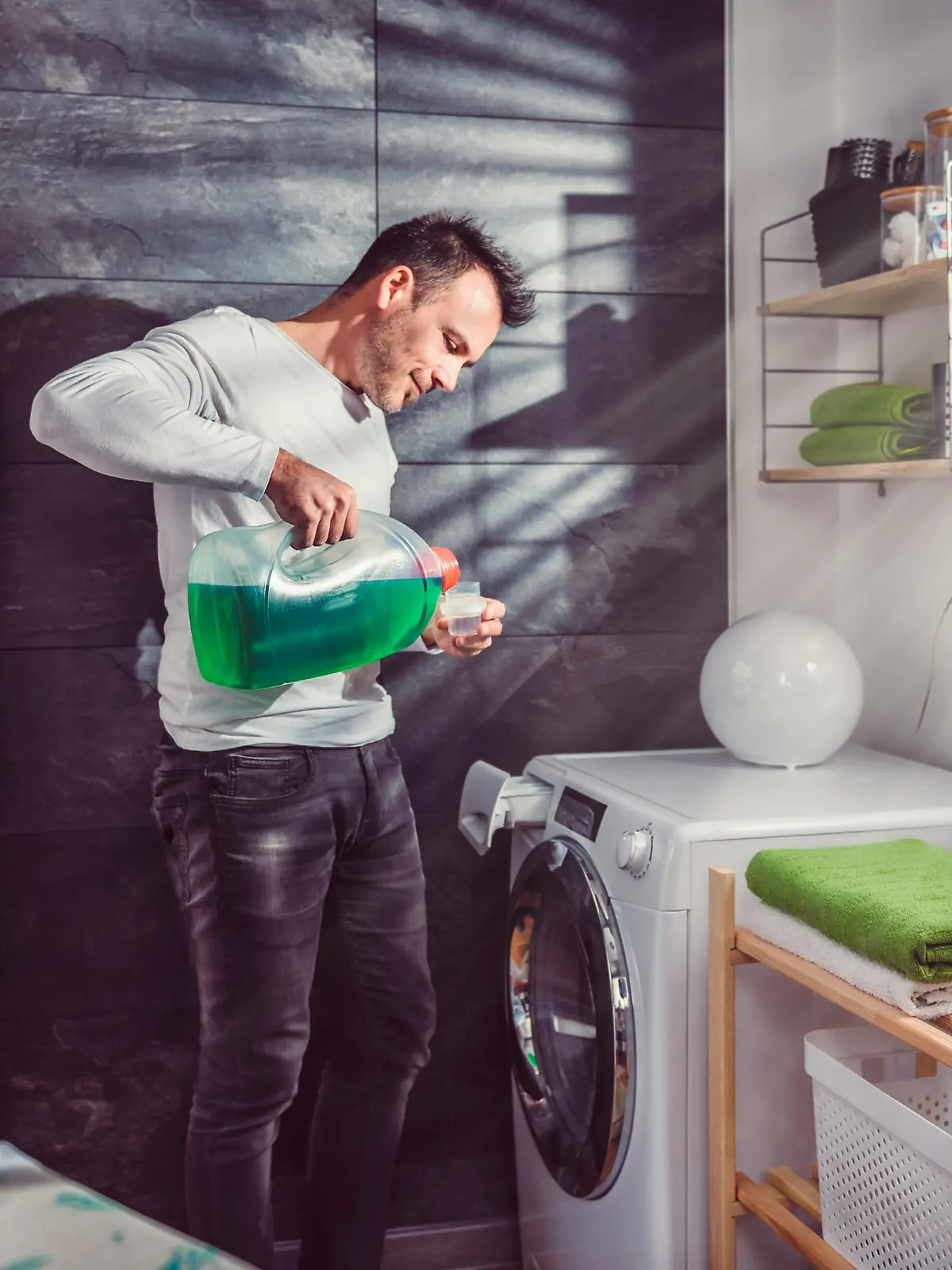 Man wearing white shirt pouring liquid laundry detergent In the bottle cap at laundry room
