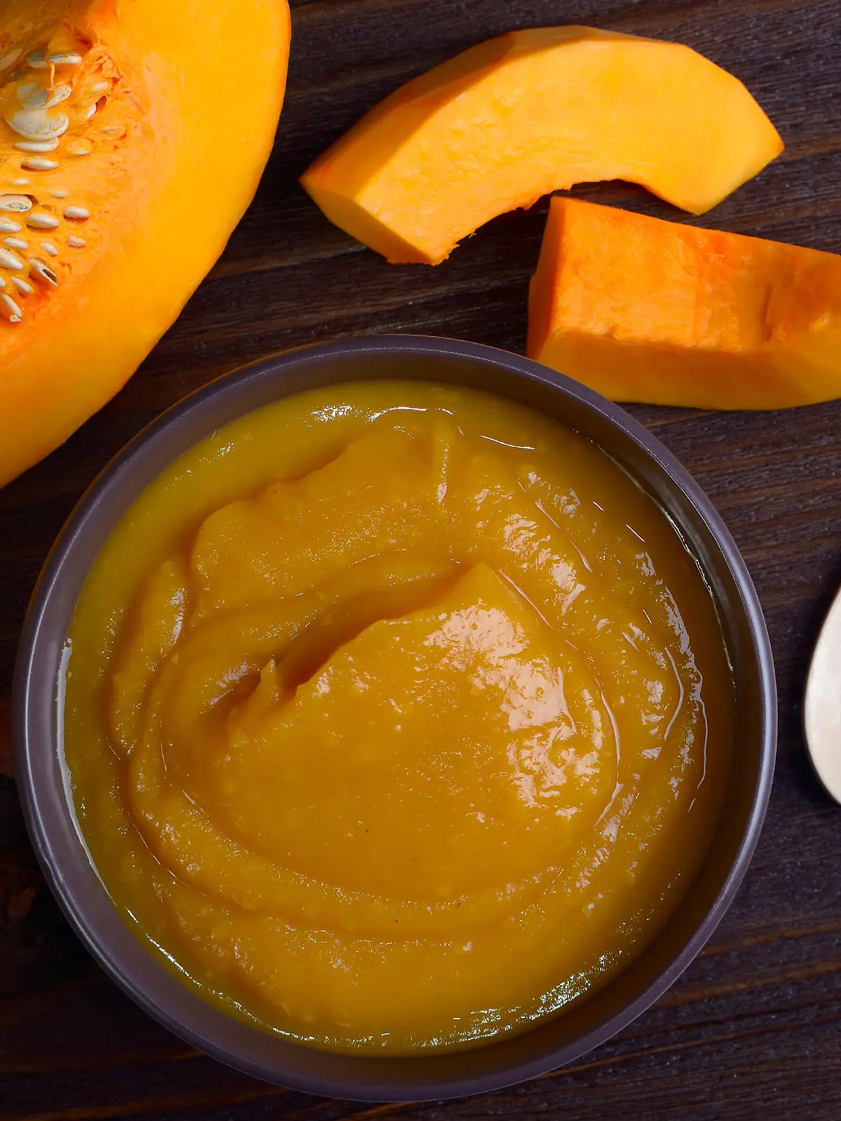 Bowl with pumpkin puree, surrounded by pieces of pumpkin, top view