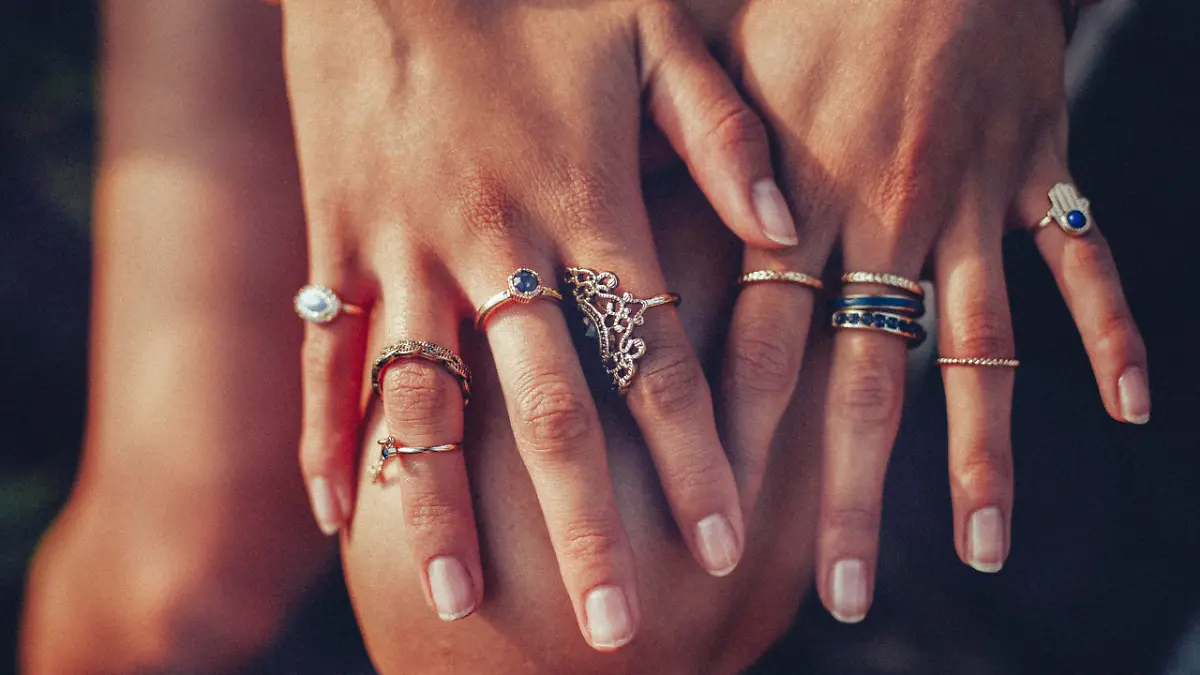 Cropped closeup of a boho girl's hands with many rings on her fingers, in gold and silver with dark blue stones