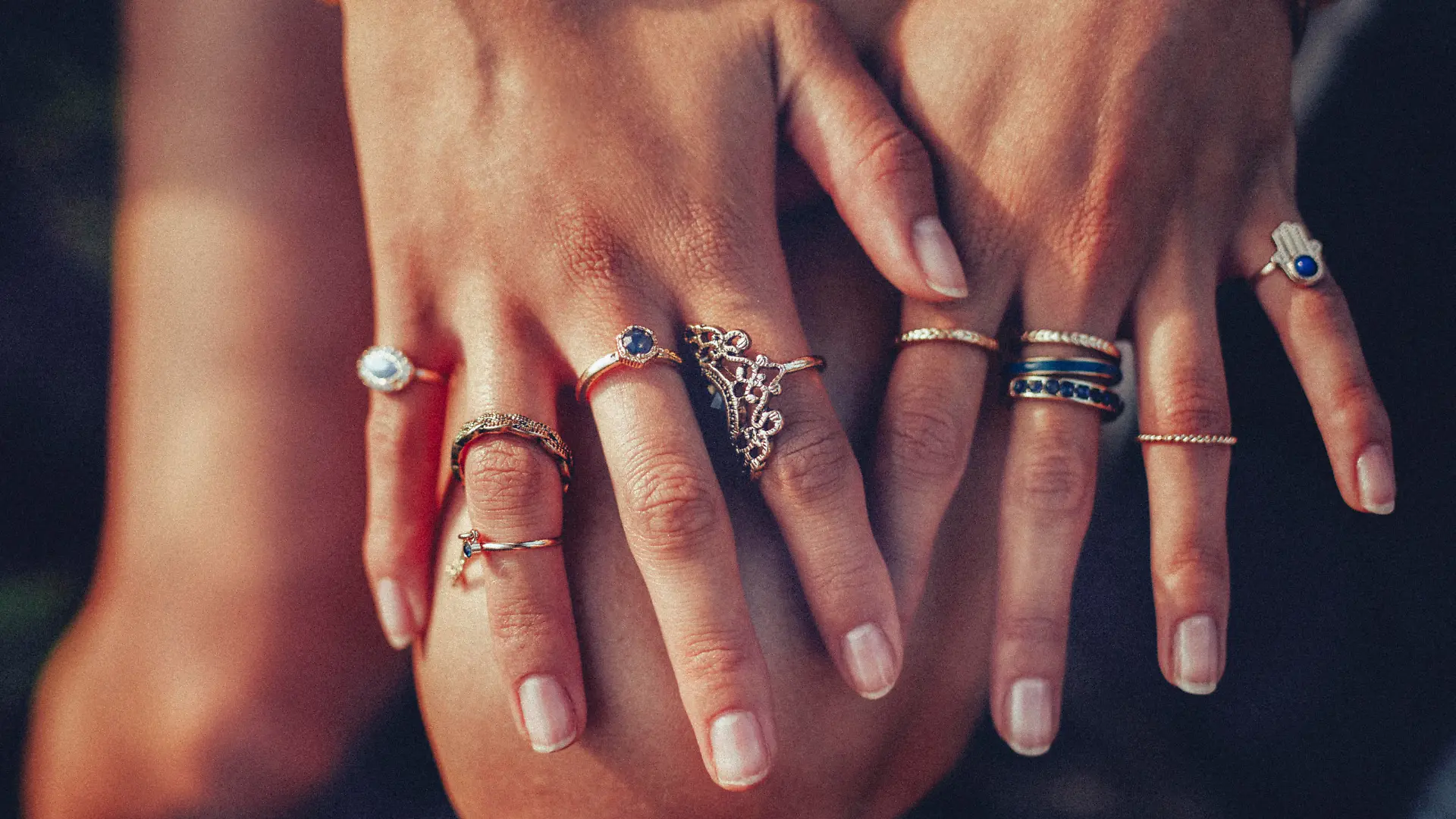 Cropped closeup of a boho girl's hands with many rings on her fingers, in gold and silver with dark blue stones