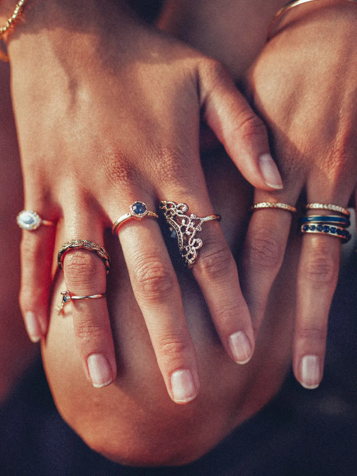 Cropped closeup of a boho girl's hands with many rings on her fingers, in gold and silver with dark blue stones