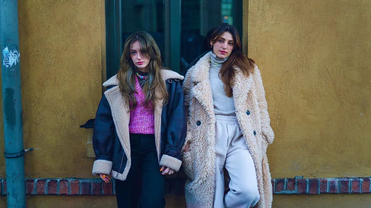Portrait of young stylish young women leaning against wall on street