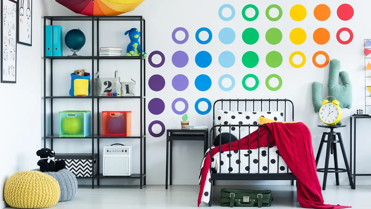 Colorful wall sticker in child's room with yellow clock on black stool and pouf on the floor