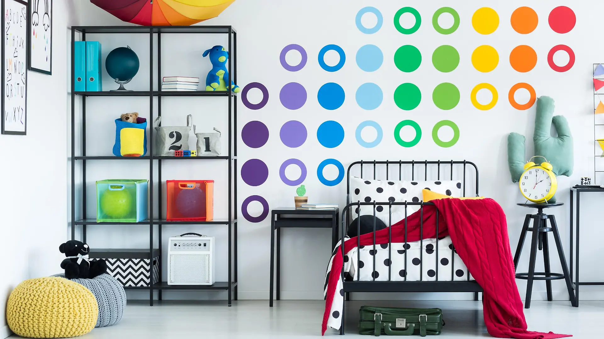Colorful wall sticker in child's room with yellow clock on black stool and pouf on the floor