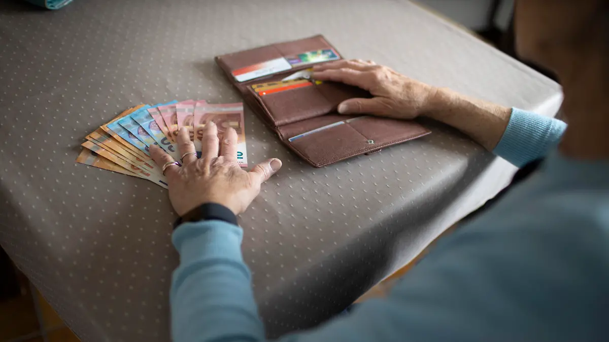 Rentnerin mit Bargeld am Kuechentisch.