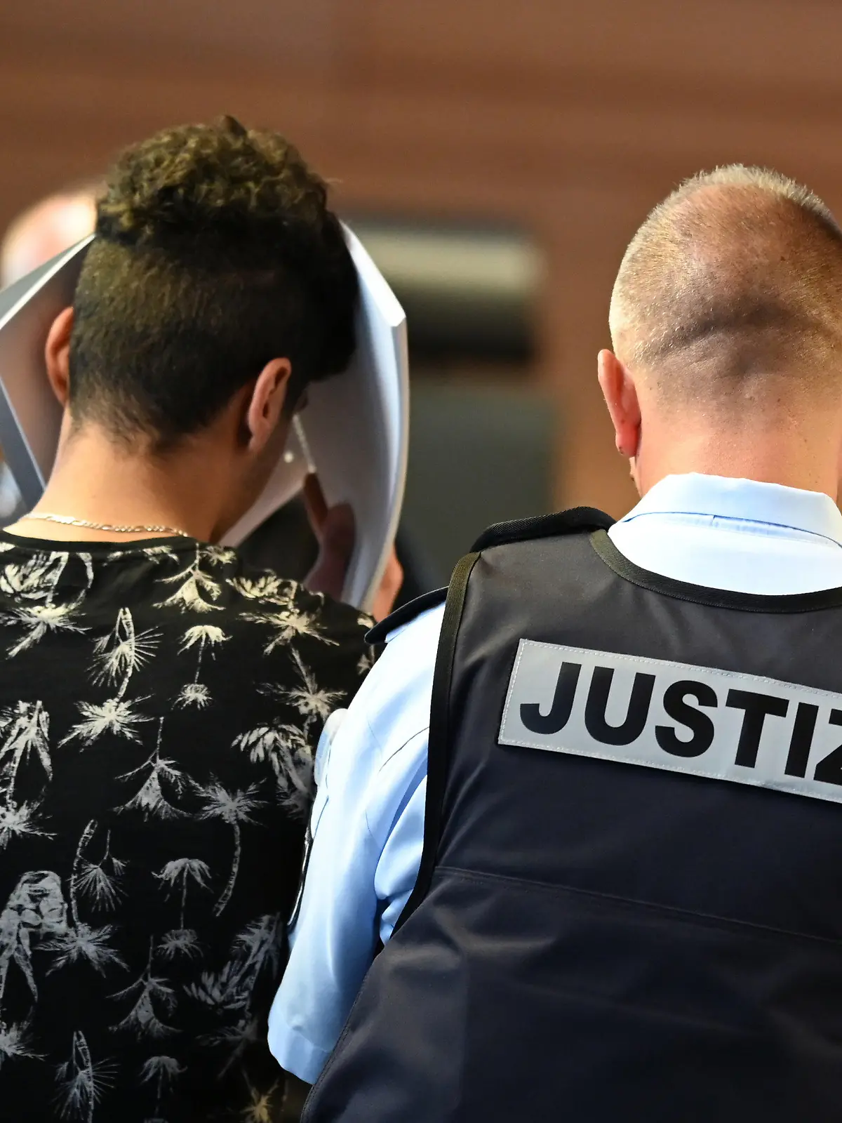 18.05.2019, Baden-Württemberg, Freiburg: Einer von elf Angeklagten wird vor dem Prozessbeginn von einem Justizbeamten in einen Gerichtssaal im Landgericht gebracht. Elf Männer sollen laut Anklage Mitte Oktober 2018 eine 18-Jährige nachts in einem Gebüsch vor einer Diskothek vergewaltigt haben. Foto: Patrick Seeger/dpa +++ dpa-Bildfunk +++