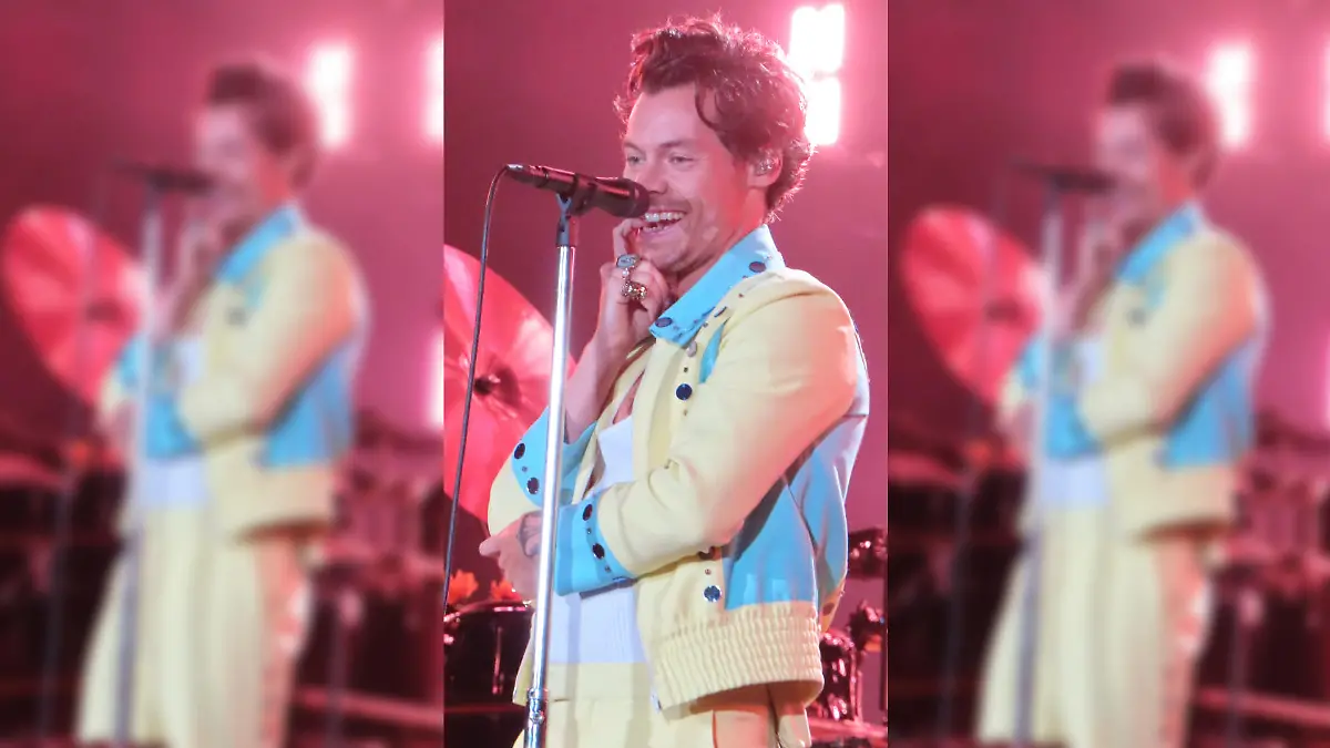 Harry Styles steht bei einem Konzert in Sydney auf der Bühne, beißt auf einen seiner Finger und grinst verschmitzt ins Publikum