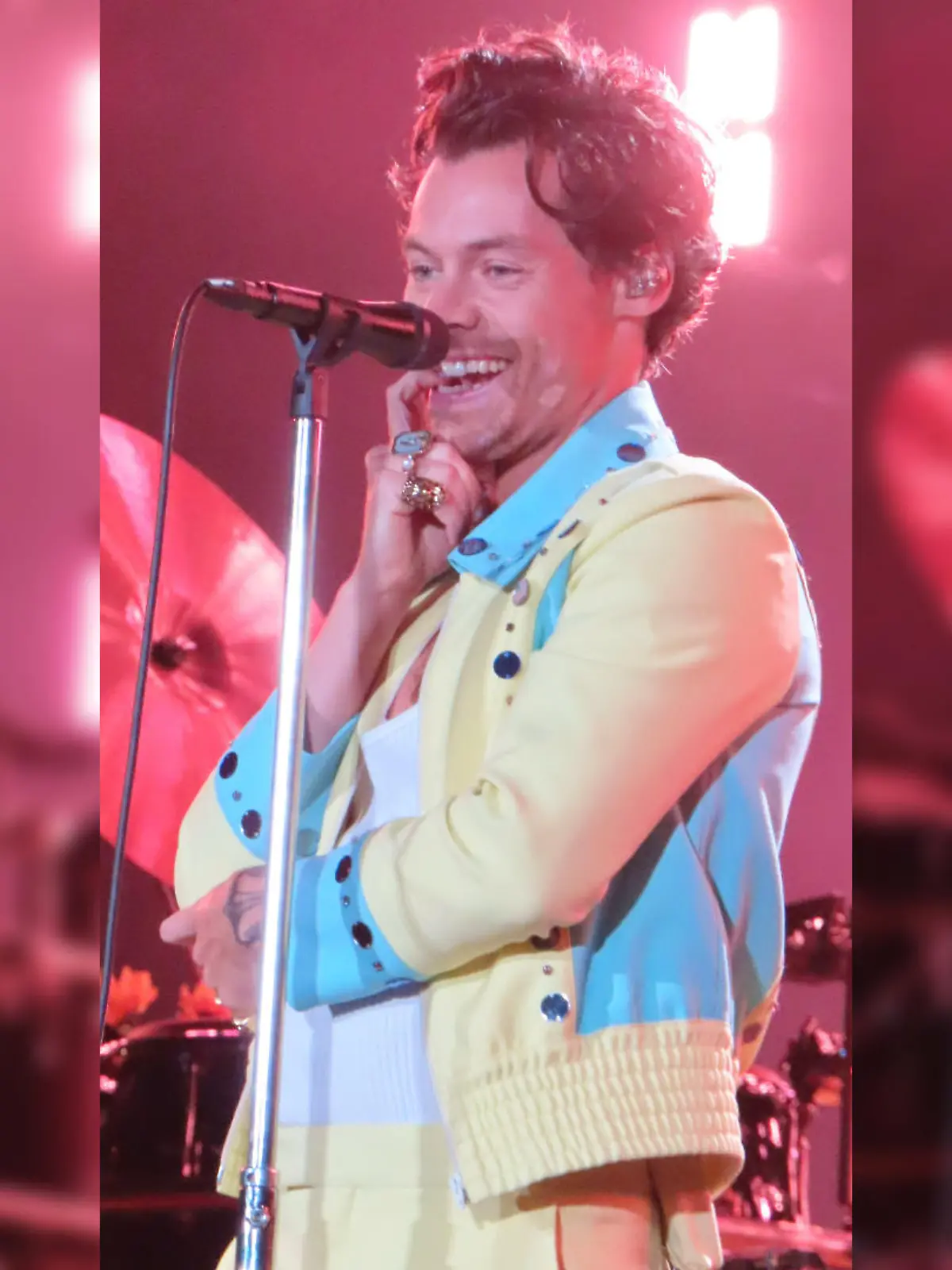 Harry Styles steht bei einem Konzert in Sydney auf der Bühne, beißt auf einen seiner Finger und grinst verschmitzt ins Publikum