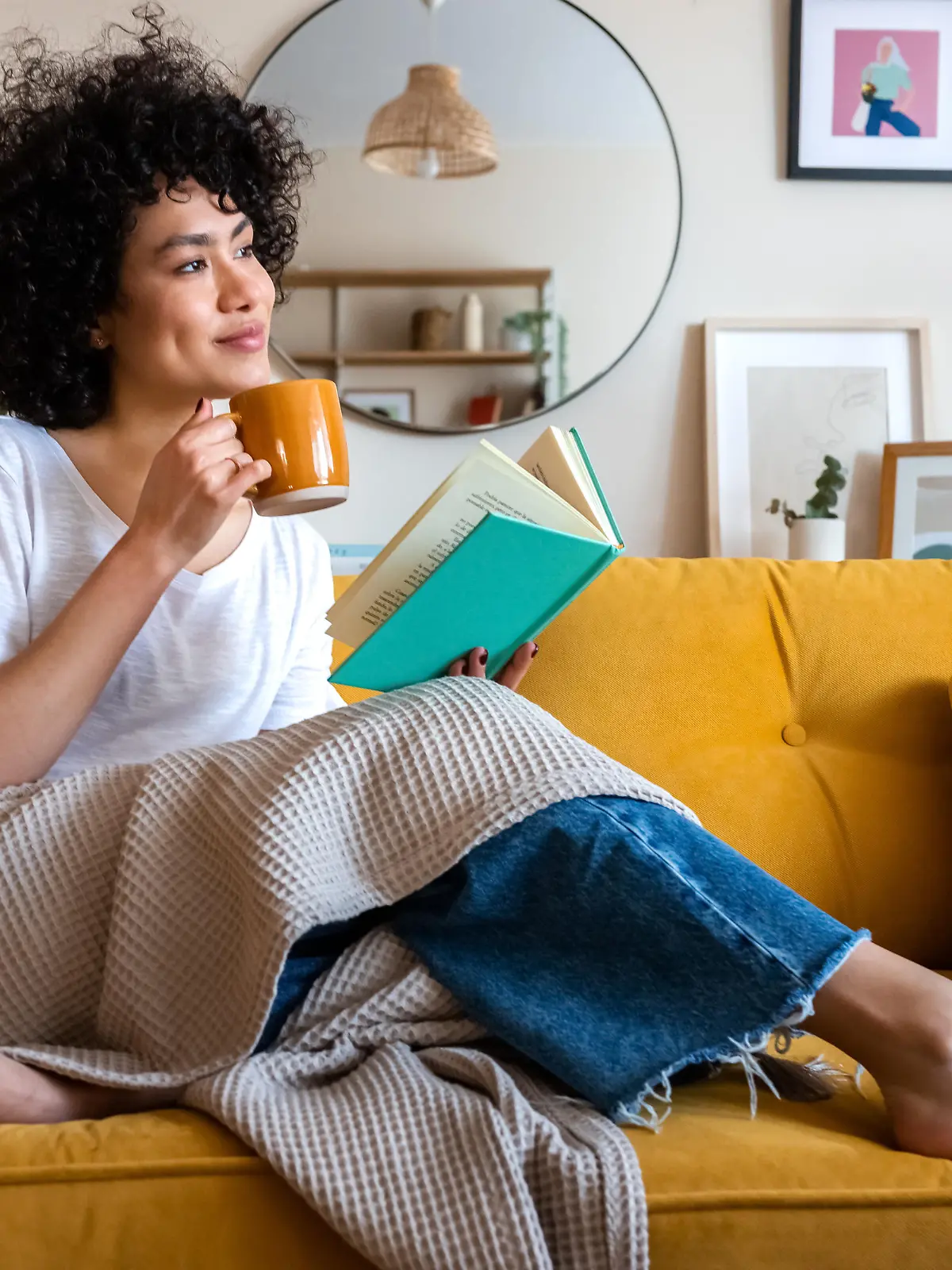 Pensive relaxed African american woman reading a book at home, drinking coffee sitting on the couch. Copy space. Lifestyle concept.