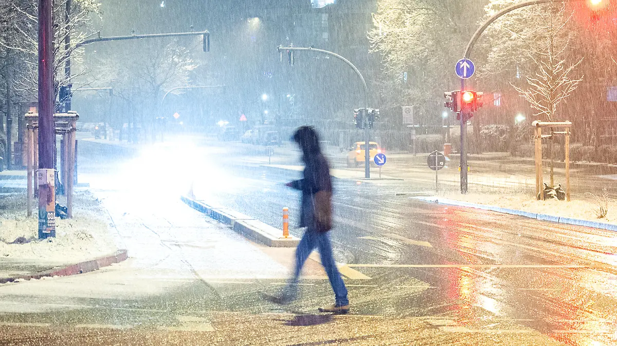 Ein Fußgänger geht am Abend bei Schneefall über eine Straße.