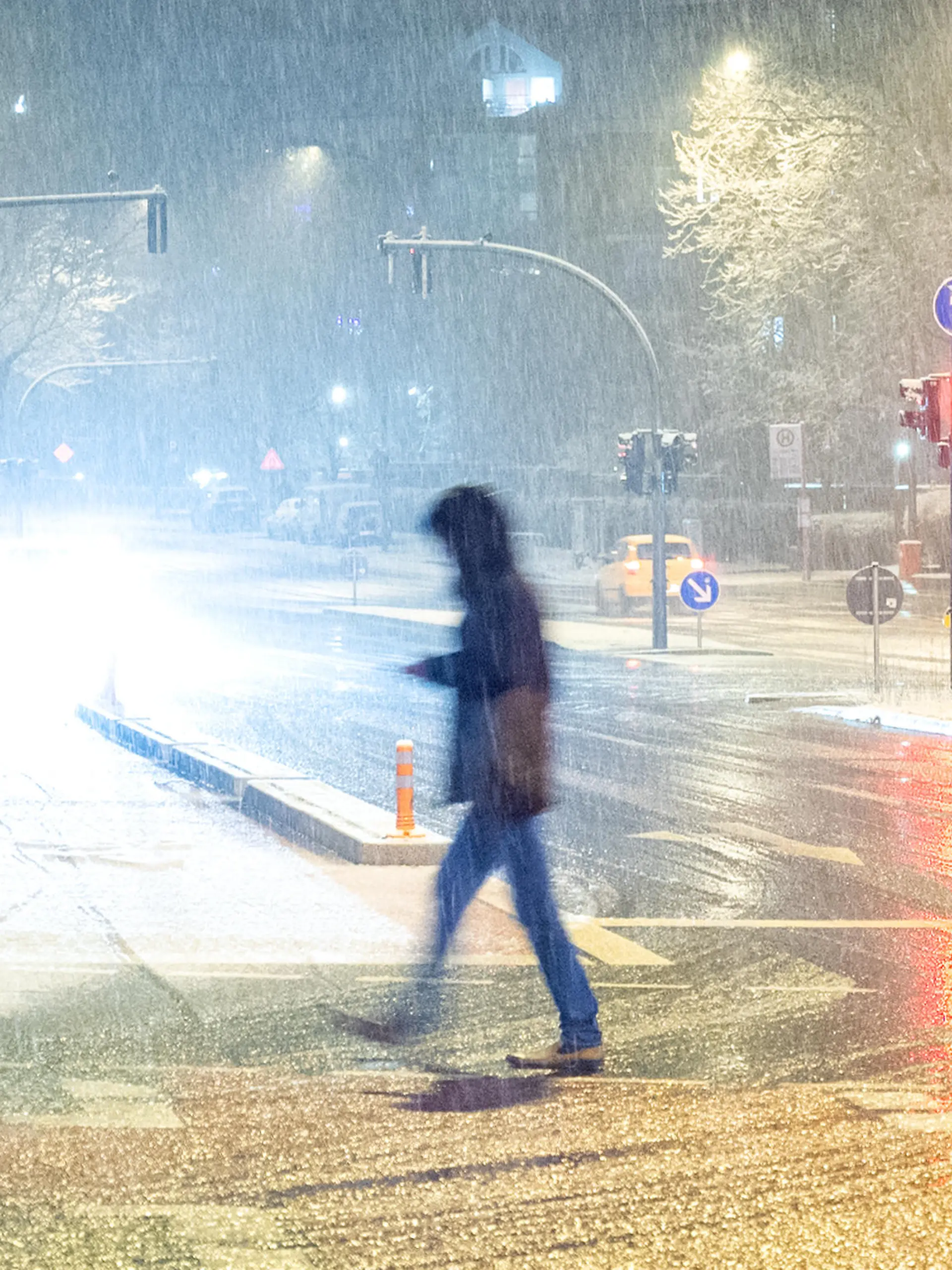 Ein Fußgänger geht am Abend bei Schneefall über eine Straße.