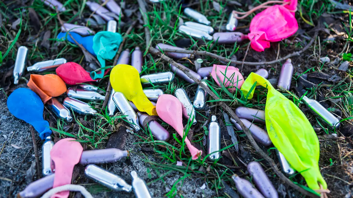 Lachgaskapseln und Luftballons liegen auf der Wiese.