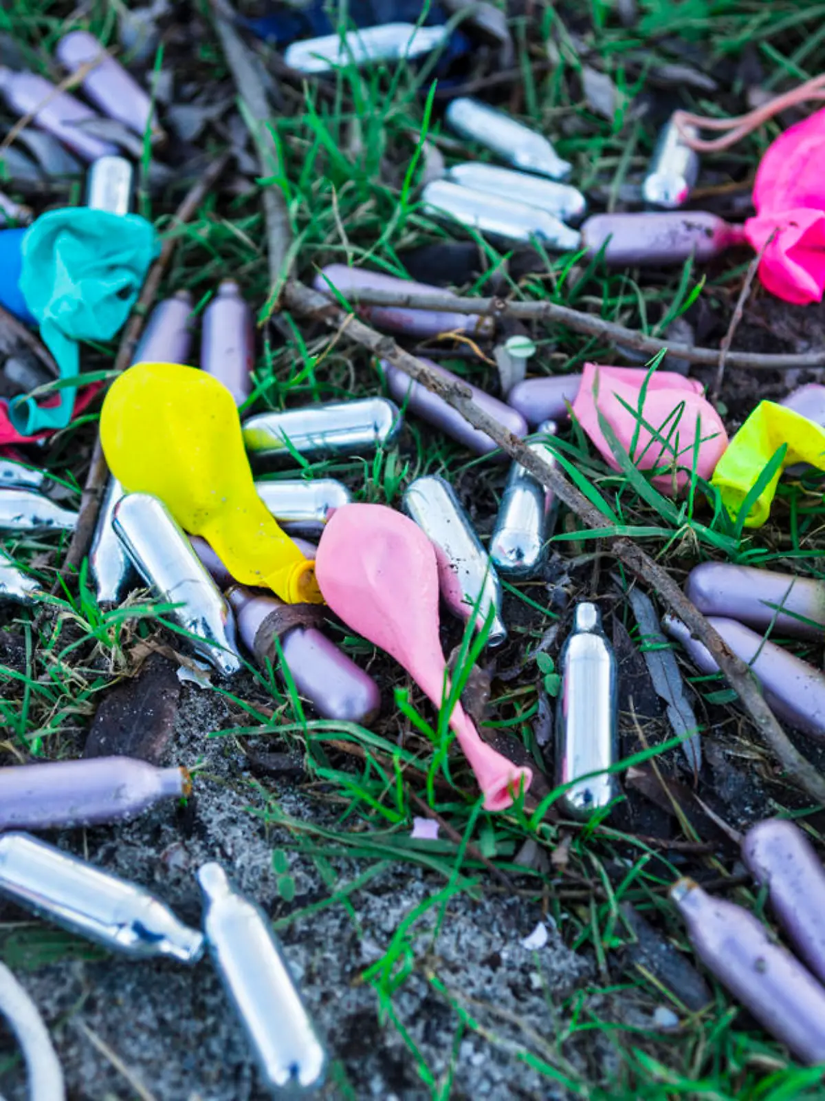 Lachgaskapseln und Luftballons liegen auf der Wiese.