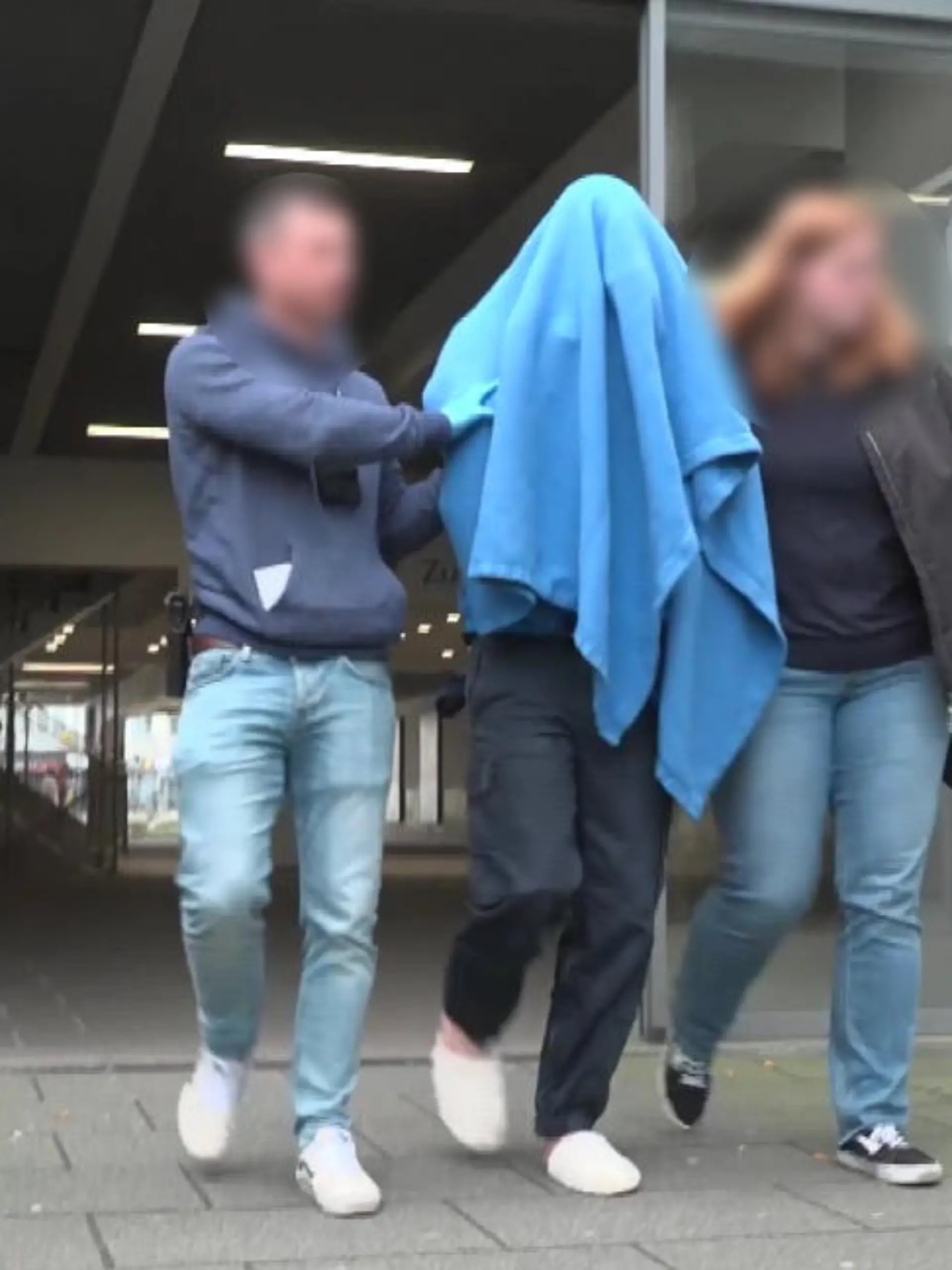 Zwei Polizisten führen den Tatverdächtigen (Mitte) aus dem Amtsgericht Osnabrück. Der 20-Jährige trägt noch Hausschuhe. Sein Gesicht verhüllt er mit einer blauen Decke.