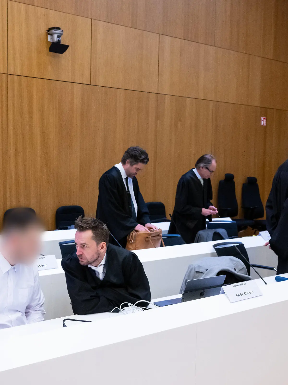 06.03.2023, Bayern, München: Die zwei wegen Mordes angeklagten Männer (2.v.l. und r) stehen vor Beginn der Verhandlung im Hochsicherheitsgerichtssaal vom Landgericht München II neben ihren Rechtsanwälten Sarah Stolle (l), Alexander Stevens (3.v.l.), Alexander Betz (4.v.l.), Patrick Ottmann (5.v.l.) und Gerhard Bink (2.v.r.). Im Prozess geht es um einen mutmaßlichen Dreifachmord in Starnberg im Januar 2020. Die beiden angeklagten Männer müssen sich wegen Mordes, besonders schweren Raubes und Verstoßes gegen das Kriegswaffenkontrollgesetz verantworten. Foto: Sven Hoppe/dpa - ACHTUNG: Person(en) wurde(n) aus rechtlichen Gründen gepixelt +++ dpa-Bildfunk +++