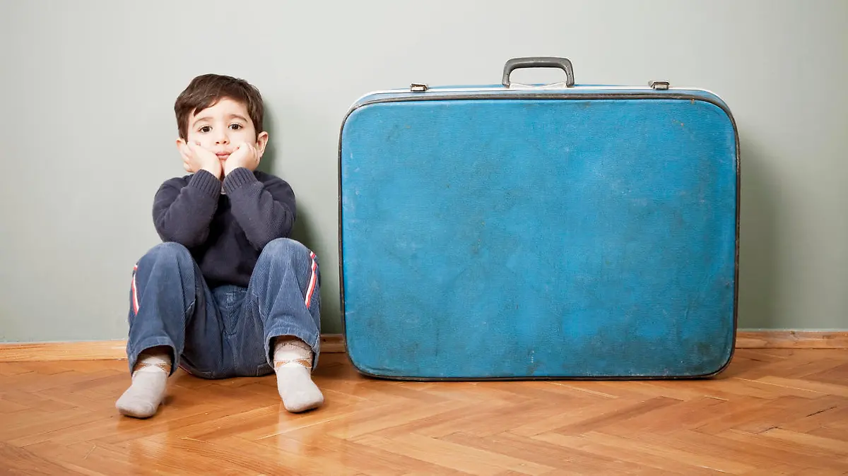 Kleiner Junge sitzt traurig neben großem Koffer