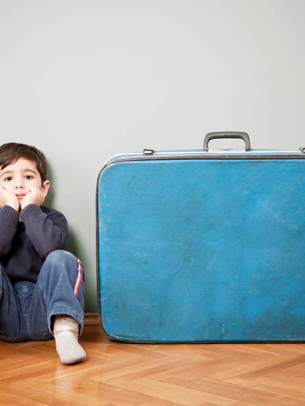 Kleiner Junge sitzt traurig neben großem Koffer