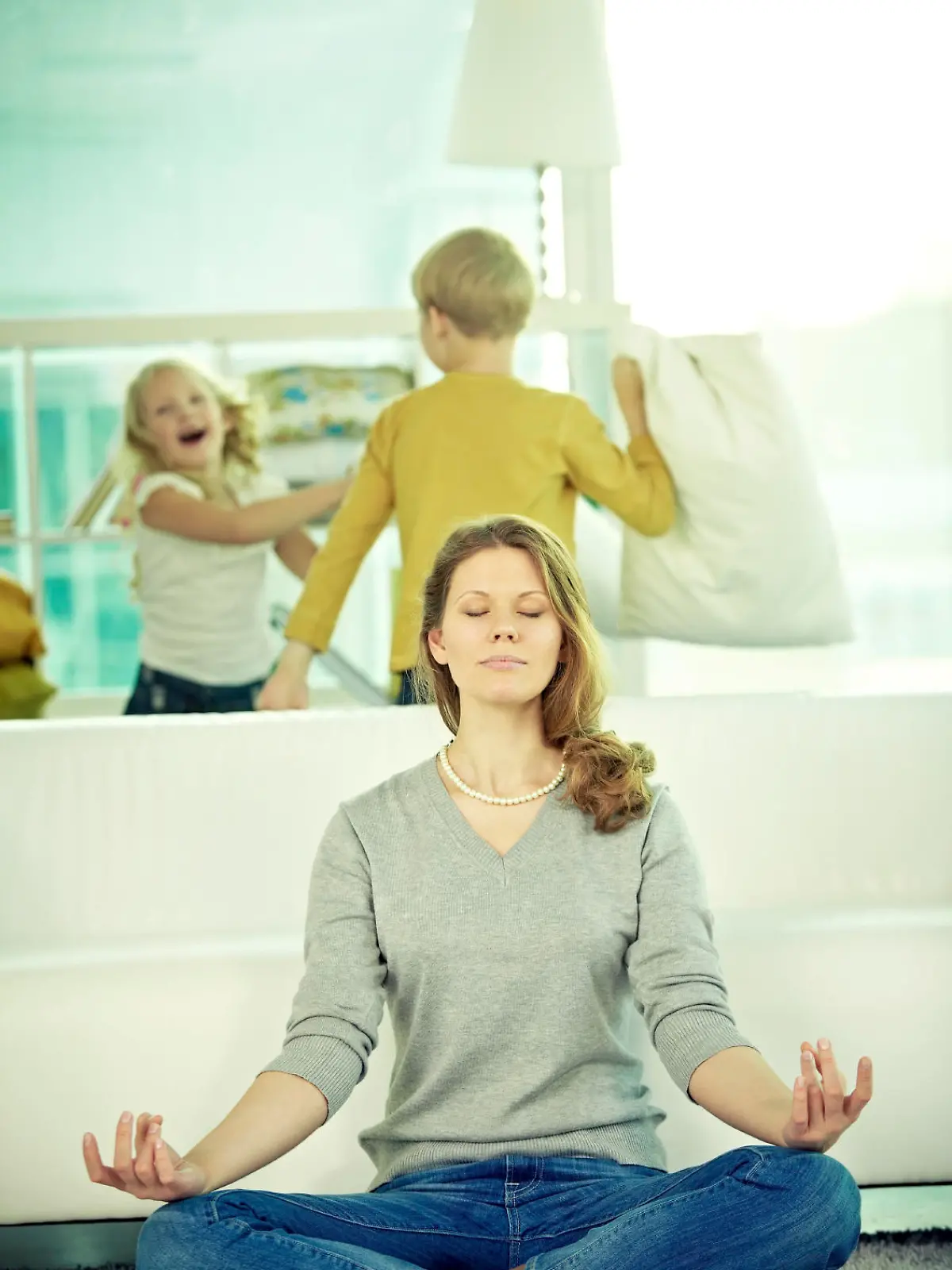 Woman meditating at home, her children playing behind