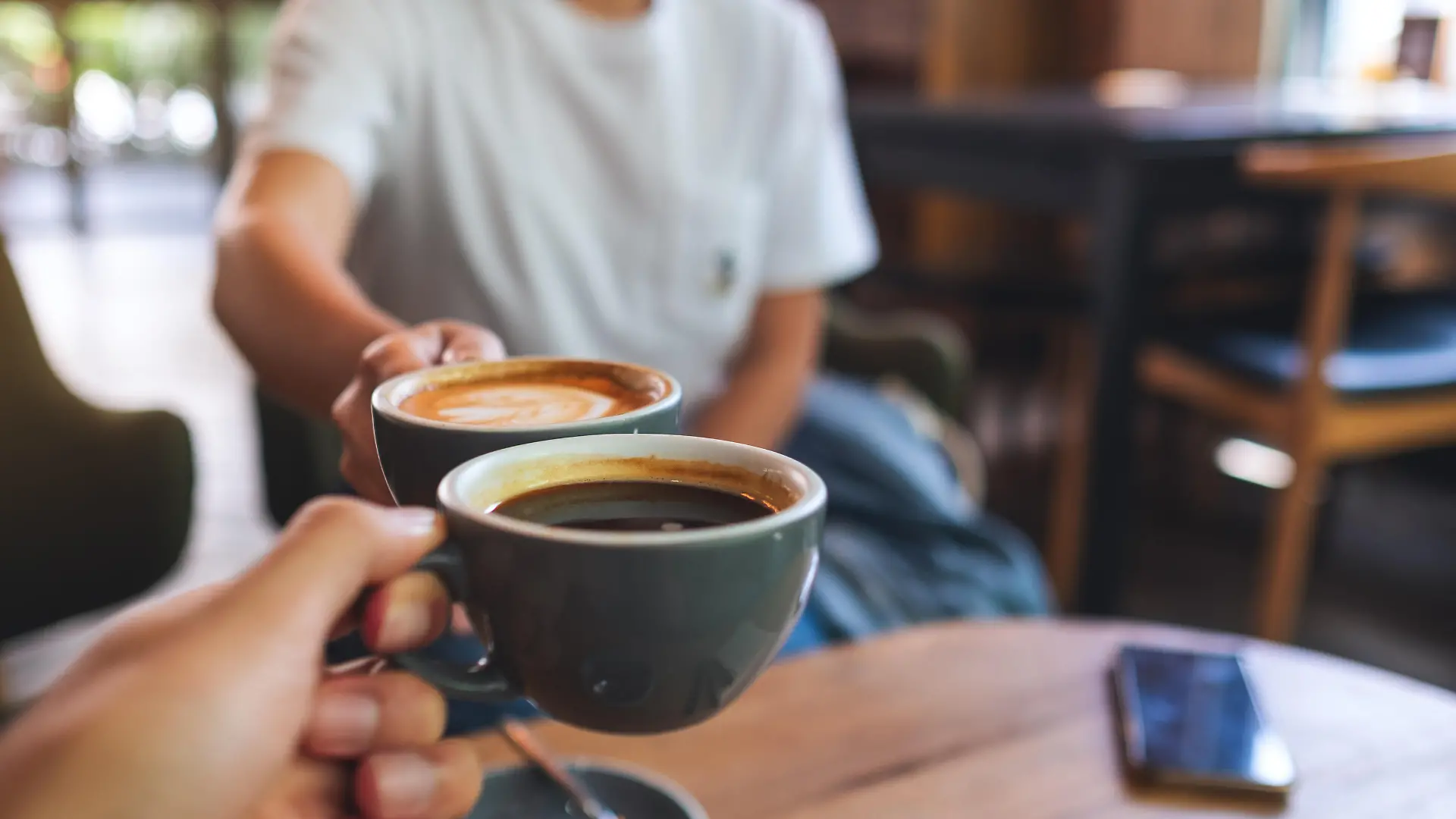 Closeup image of a man and a woman clinking coffee mugs in cafe