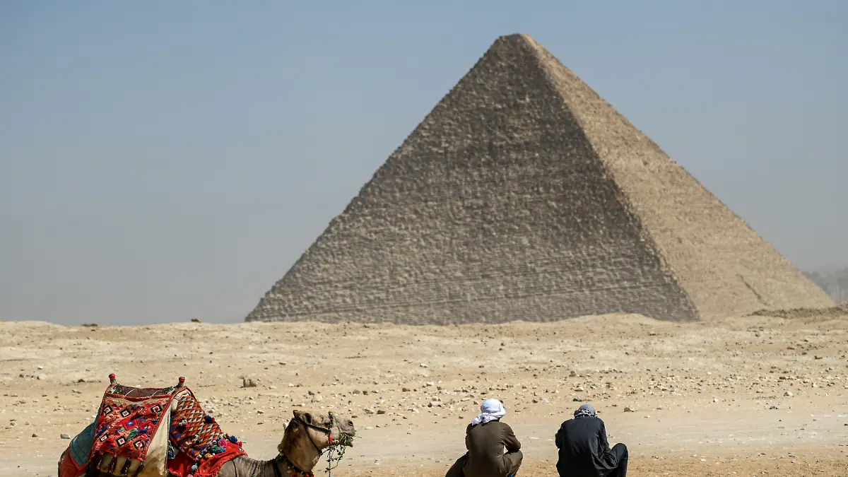 dpatopbilder - 02.03.2023, Ägypten, Gizeh: Ein Kamel und seine Reiter rasten vor der Großen Pyramide von Gizeh. Ein internationales Forschungsteam hat in der berühmten ägyptischen Cheops-Pyramide von Gizeh eine bisher unbekannte Kammer nachgewiesen. Foto: Sayed Hassan/dpa +++ dpa-Bildfunk +++