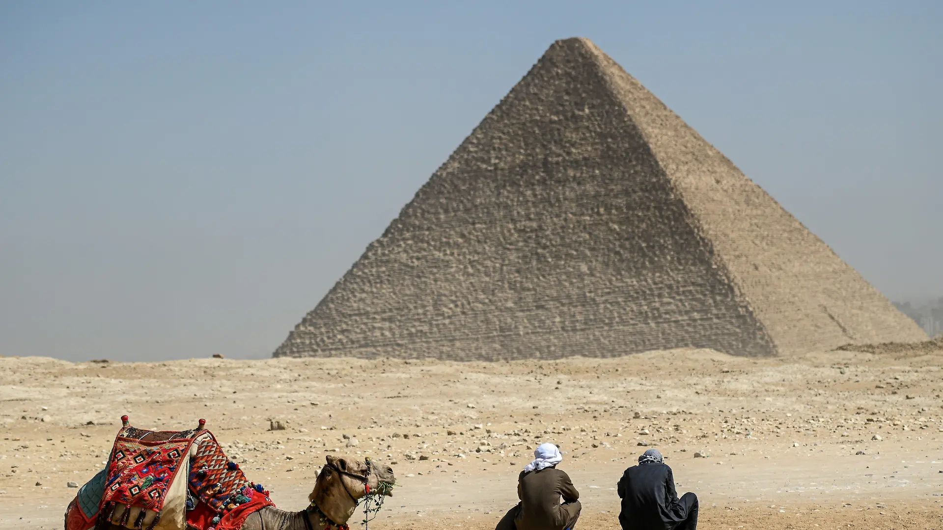 dpatopbilder - 02.03.2023, Ägypten, Gizeh: Ein Kamel und seine Reiter rasten vor der Großen Pyramide von Gizeh. Ein internationales Forschungsteam hat in der berühmten ägyptischen Cheops-Pyramide von Gizeh eine bisher unbekannte Kammer nachgewiesen. Foto: Sayed Hassan/dpa +++ dpa-Bildfunk +++