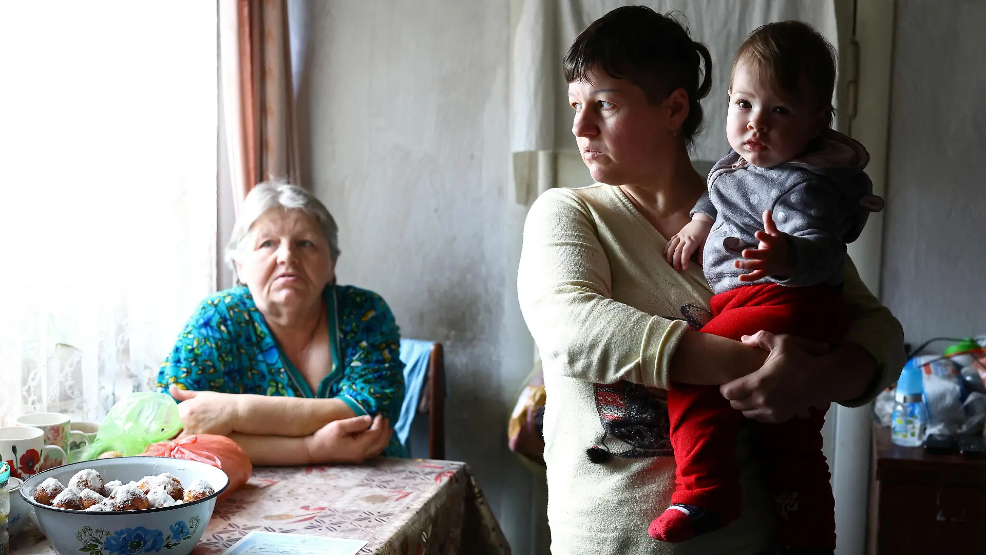 Natalia Lukina looks out the window as she holds her baby Kateryna, who was born during the Russian occupation, next to her mother Olha inside their house just 1.5 kilometers away from Russian positions across the Dnipro river, amid Russia's invasion of Ukraine, in Antonivka, Kherson region, Ukraine, February 23, 2023. REUTERS/Lisi Niesner