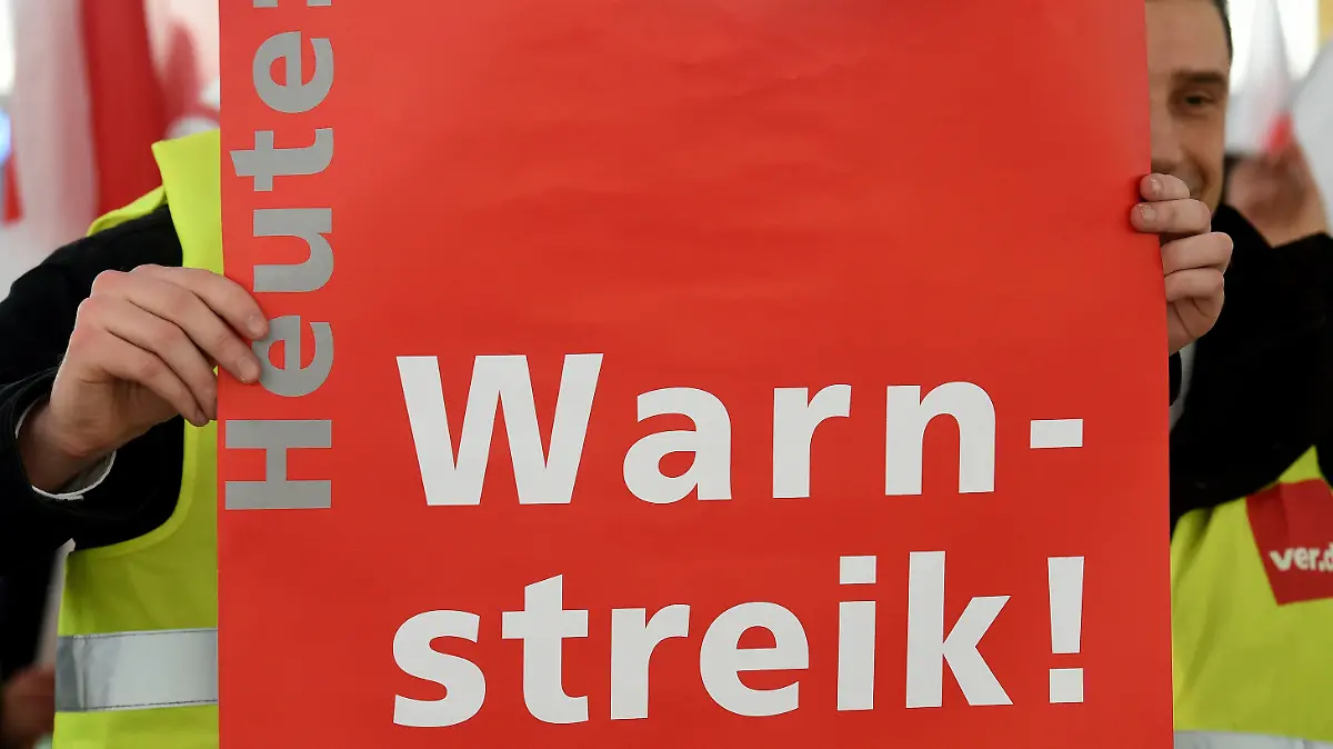 ARCHIV - Mit einem Plakat steht ein Mitarbeiter der Fluggast-, Personal- und Warenkontrolle am 30.01.2015 in einer Abflughalle des Flughafens Hannover (Niedersachsen). Foto: Holger Hollemann/dpa  (zu dpa: "Gewerkschaften stimmen auf Warnstreiks im öffentlichen Dienst ein" vom 26.02.2015) +++(c) dpa - Bildfunk+++